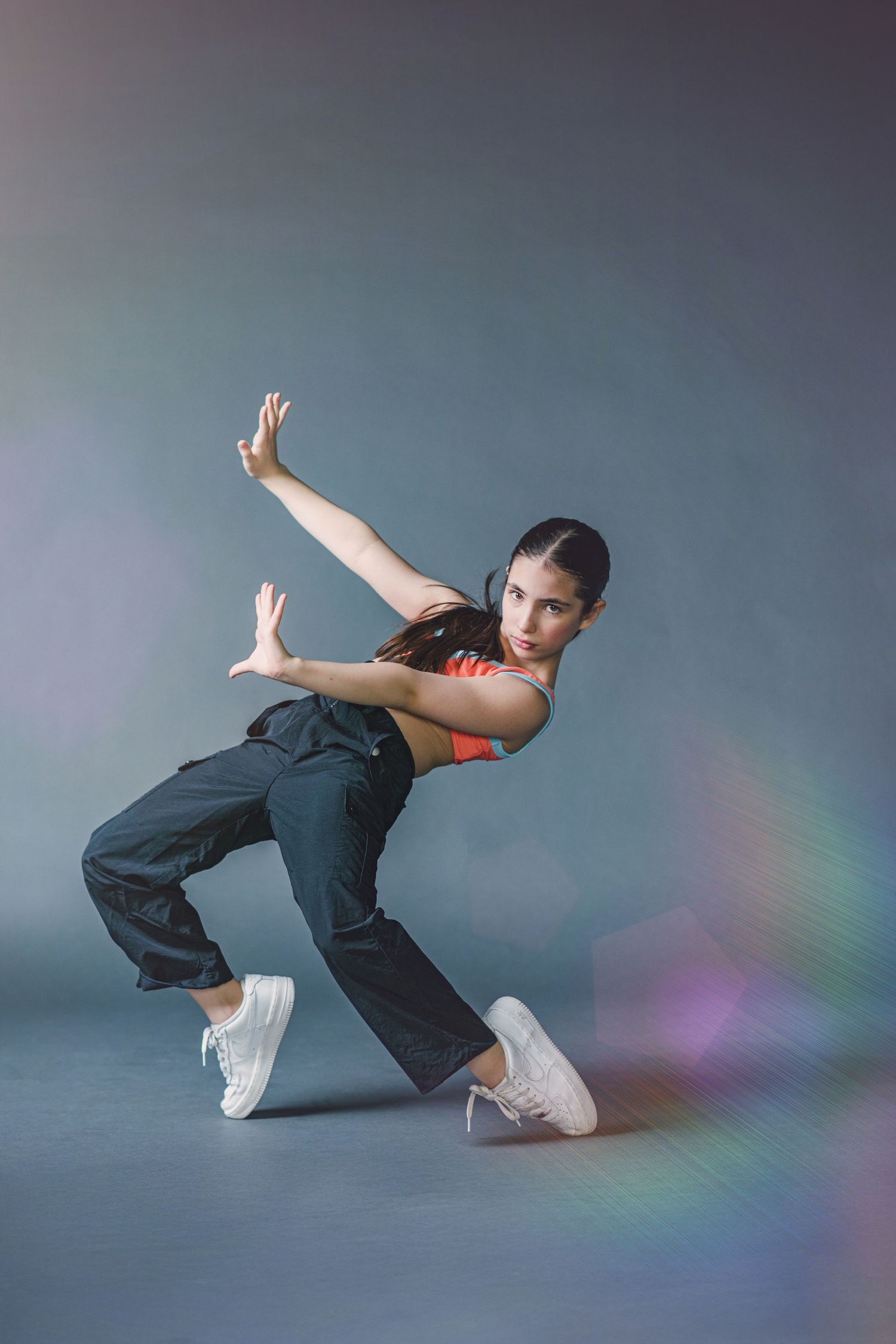 Dancer in casual wear performs contemporary dance moves against a gray backdrop with rainbow light effects.