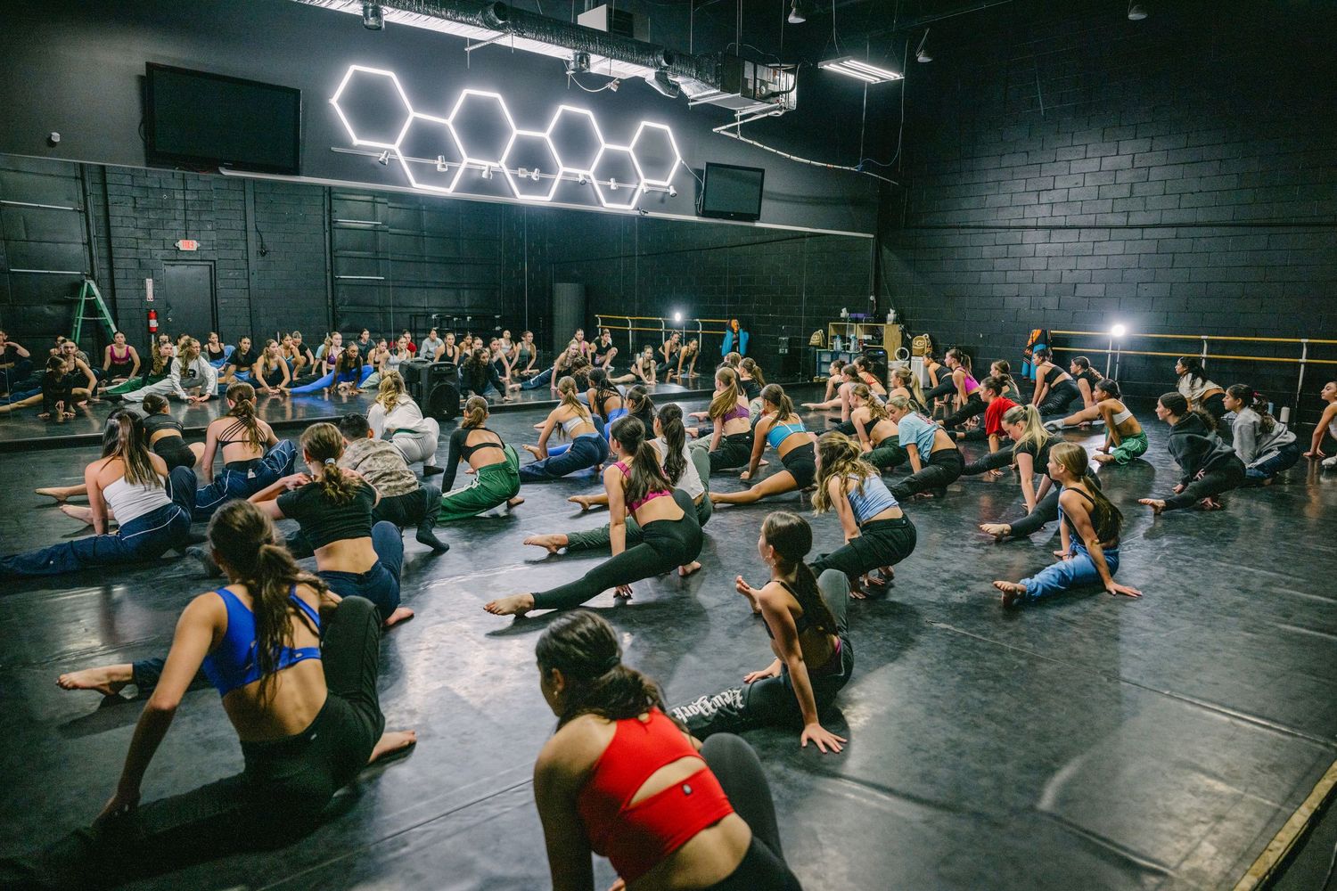 Group fitness participants exercise on yoga mats in a dimly lit studio with neon lighting.