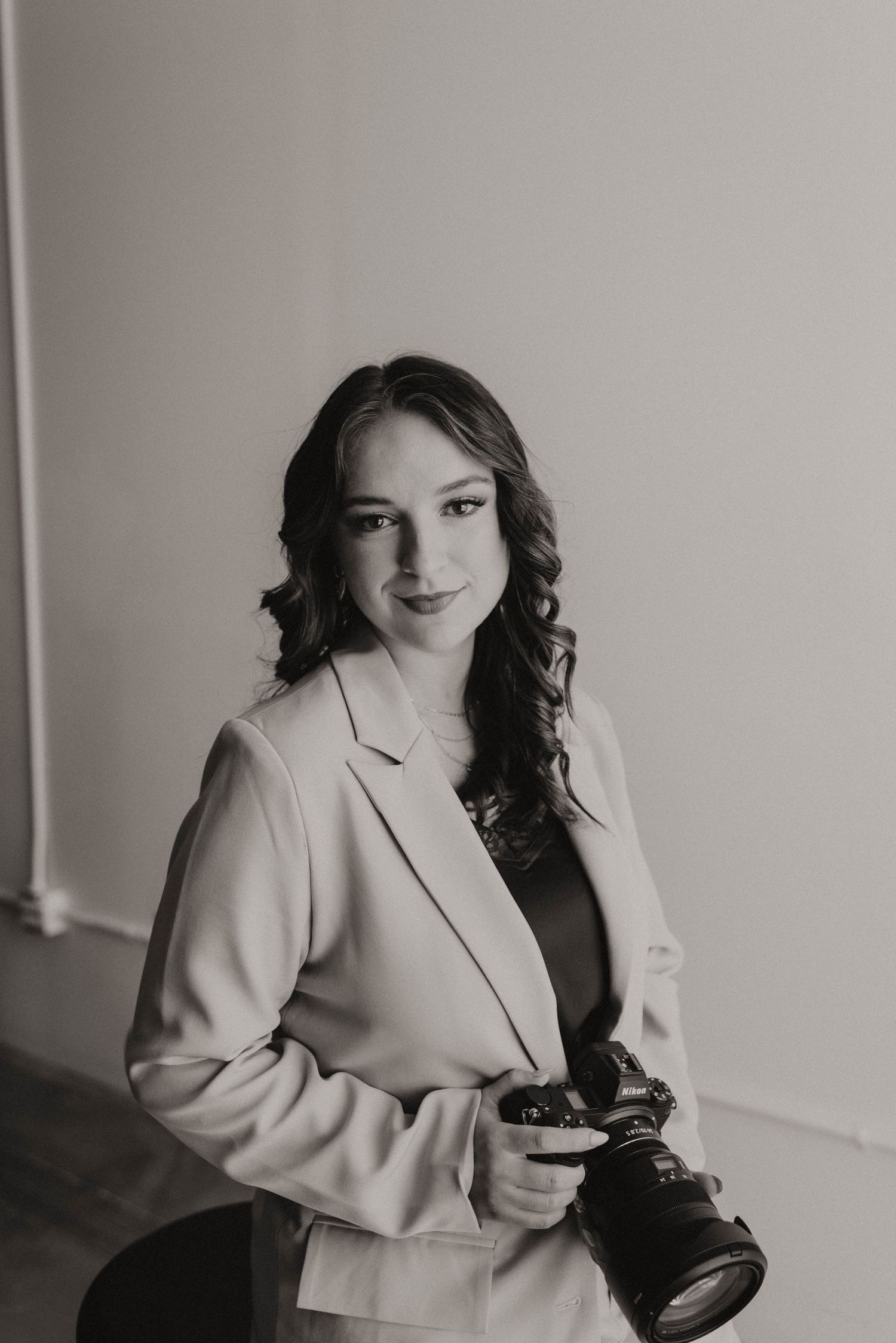 A series of black and white photographs showing a person in a light colored blazer posing with a camera against a wall.
