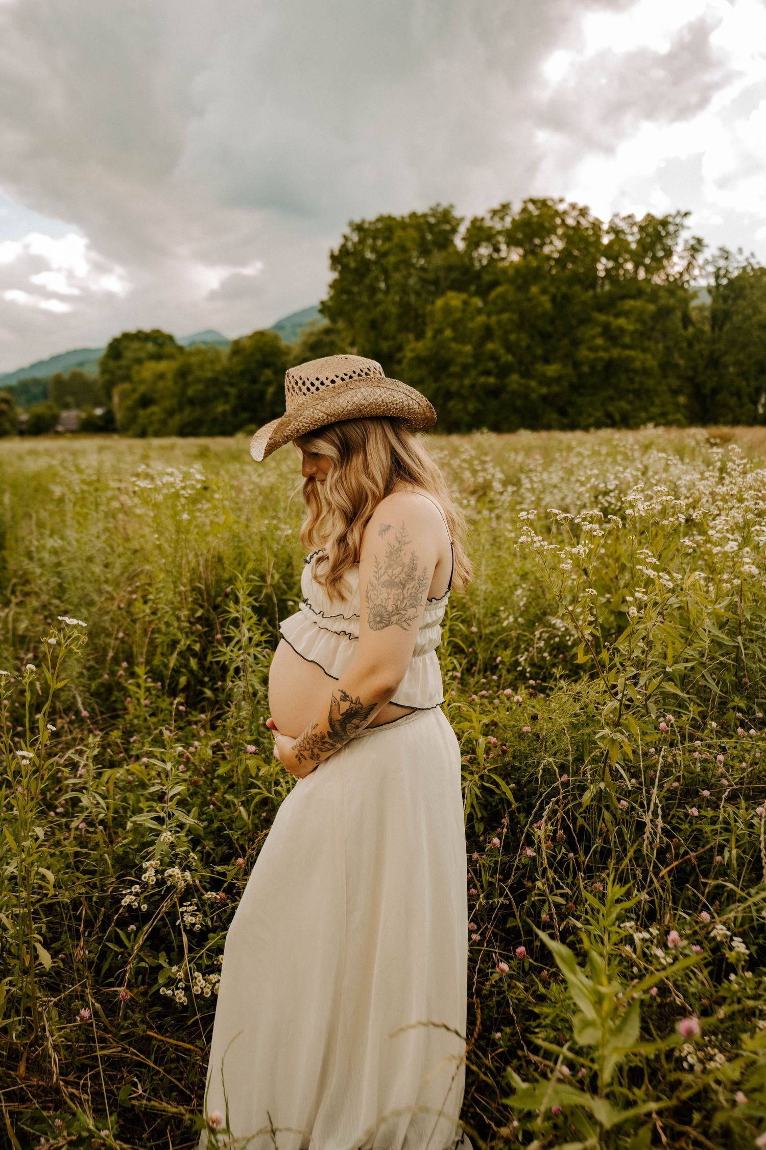 A couple in a white dress and hat share an intimate moment together in a wildflower meadow at sunset.