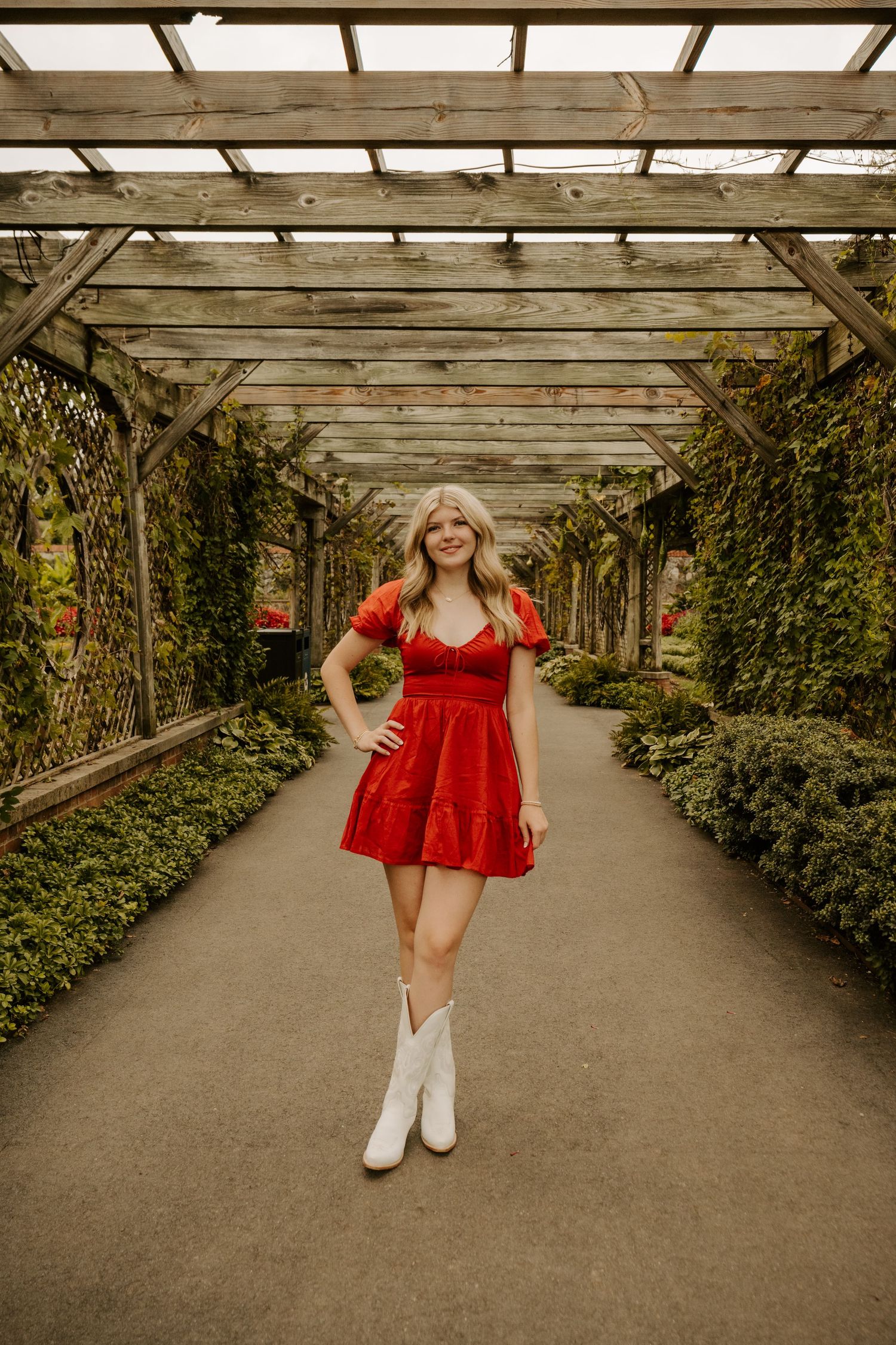 A series of photos showing a person in a red dress and white boots walking through a rustic greenhouse walkway.