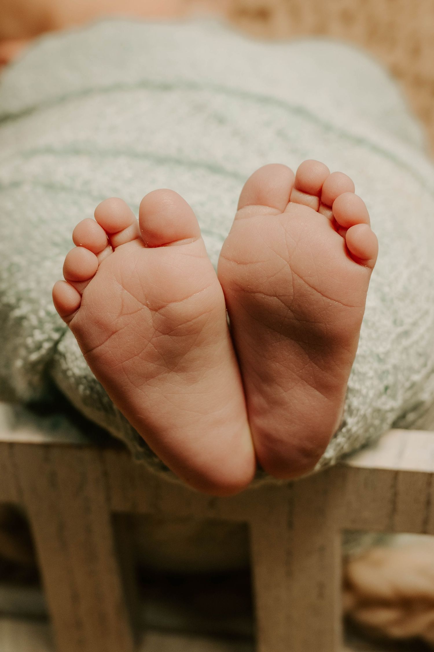 Close-up of tiny baby feet wrapped in soft mint green blanket resting on wooden surface in warm lighting.