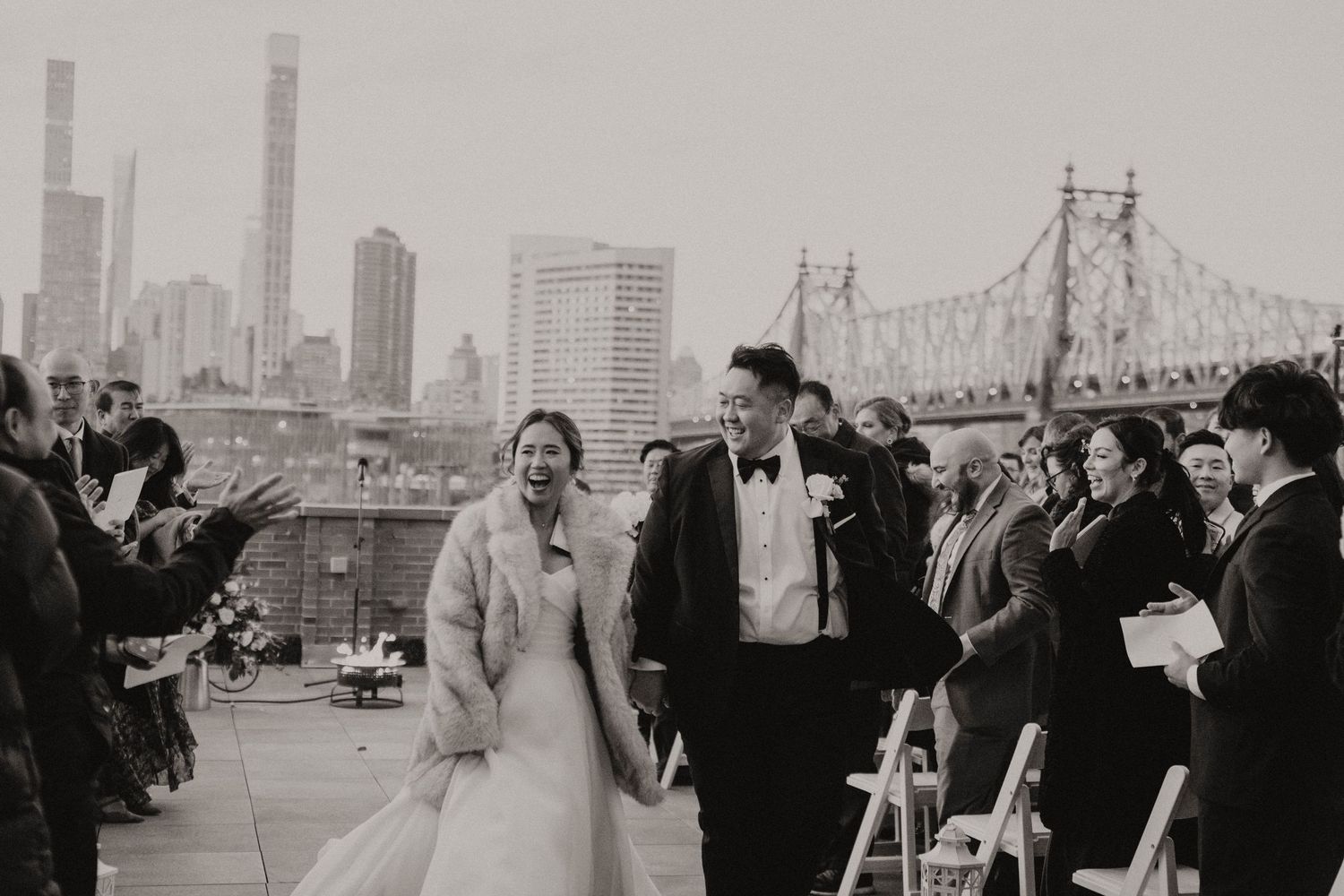 A black and white panoramic view of a city skyline with a bridge and people gathered in the foreground.