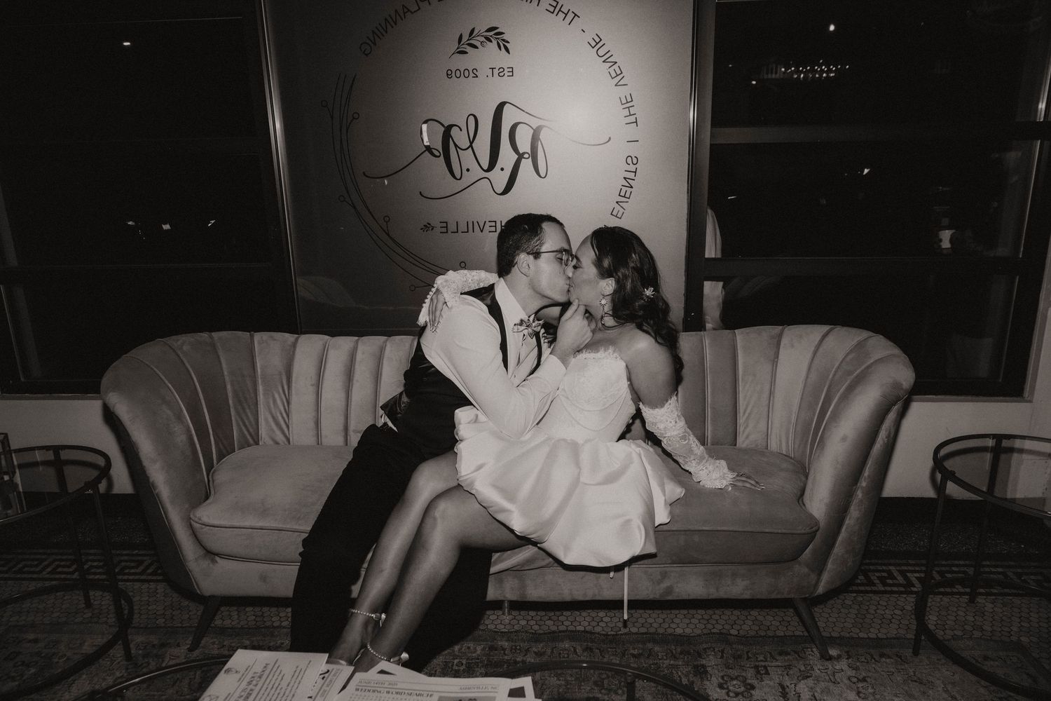 Elegant black and white vintage-style photo of a romantic couple sharing a tender moment on an antique velvet couch.