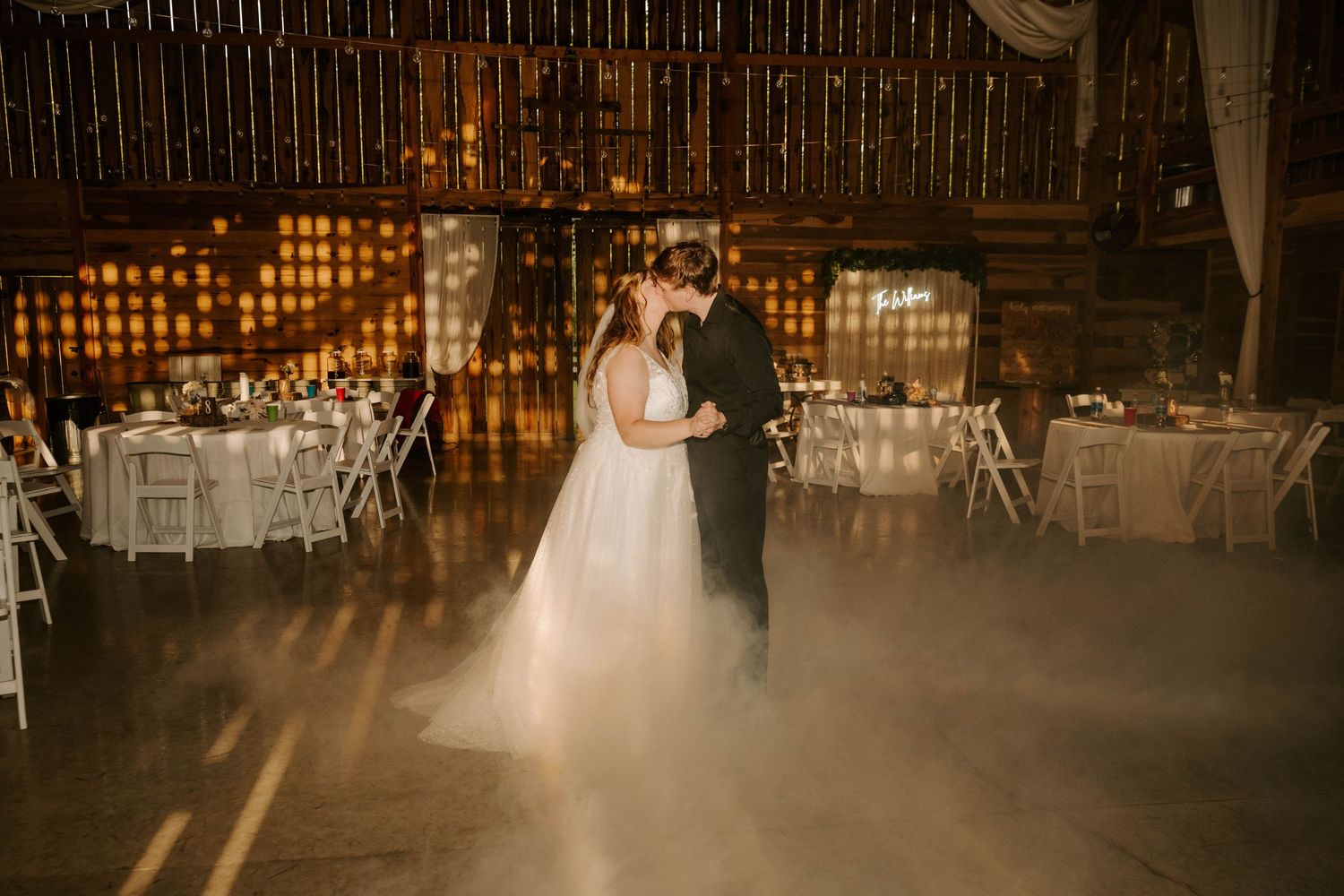 A romantic first dance in a rustic barn venue with dreamy fog and warm glowing lights.