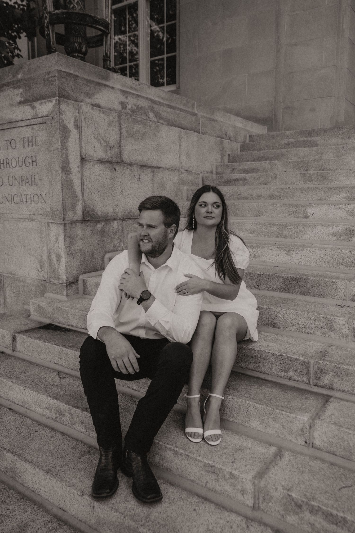 Couple in black and white sitting on stone steps with formal attire during an engagement photo session.