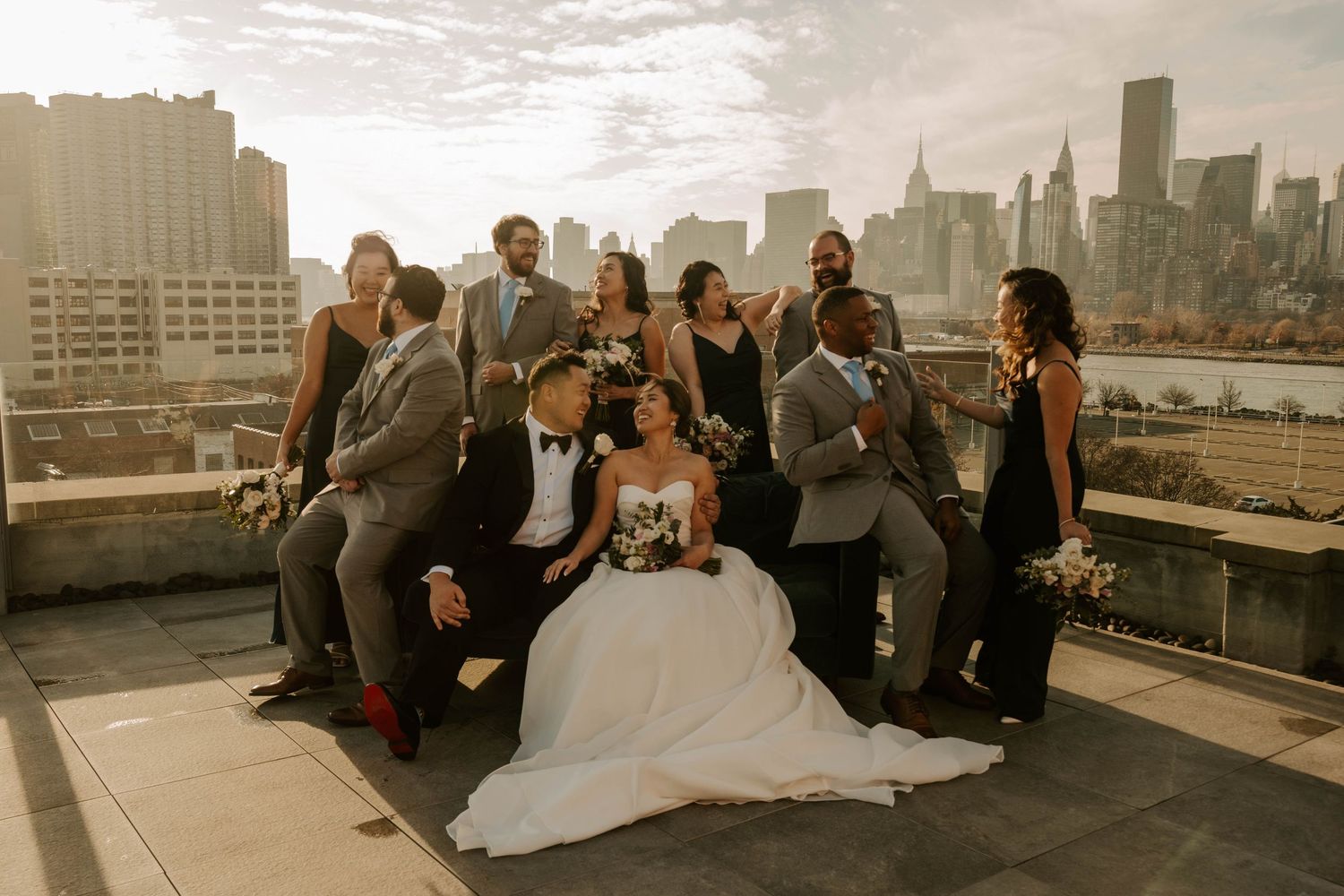 Wedding party poses together on a rooftop terrace with the New York City skyline visible in the background.