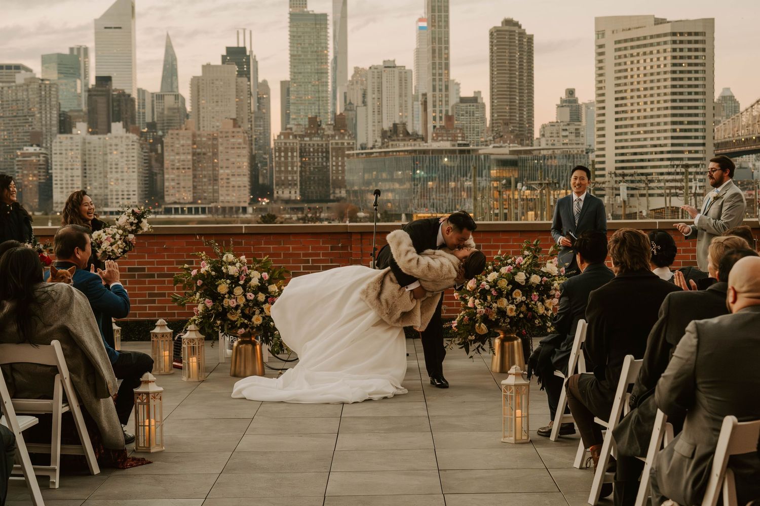 Newlyweds share a romantic dip during their rooftop wedding ceremony with Manhattan skyscrapers in view.