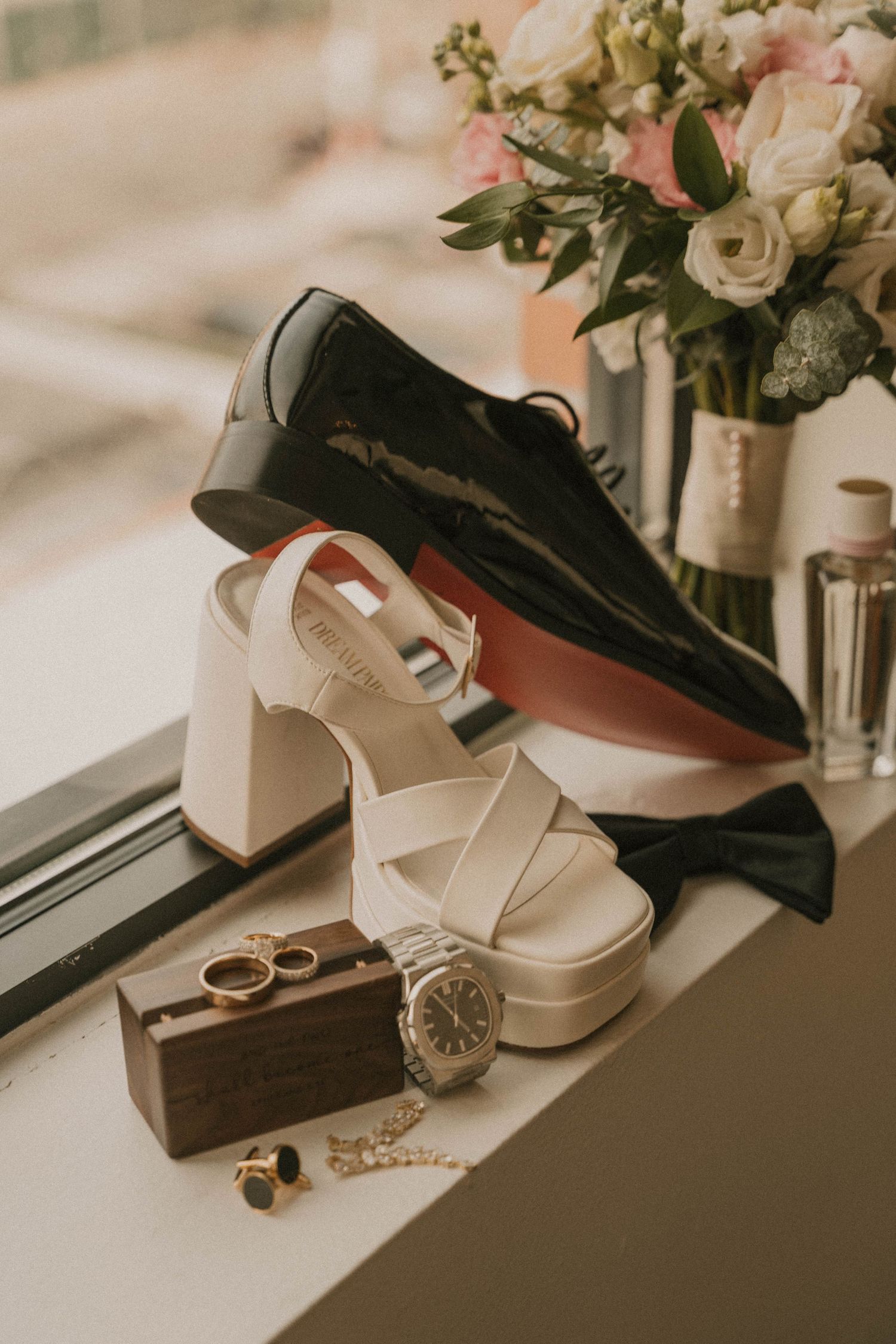 Wedding accessories including white shoes, rings, and floral arrangements displayed on a light surface.