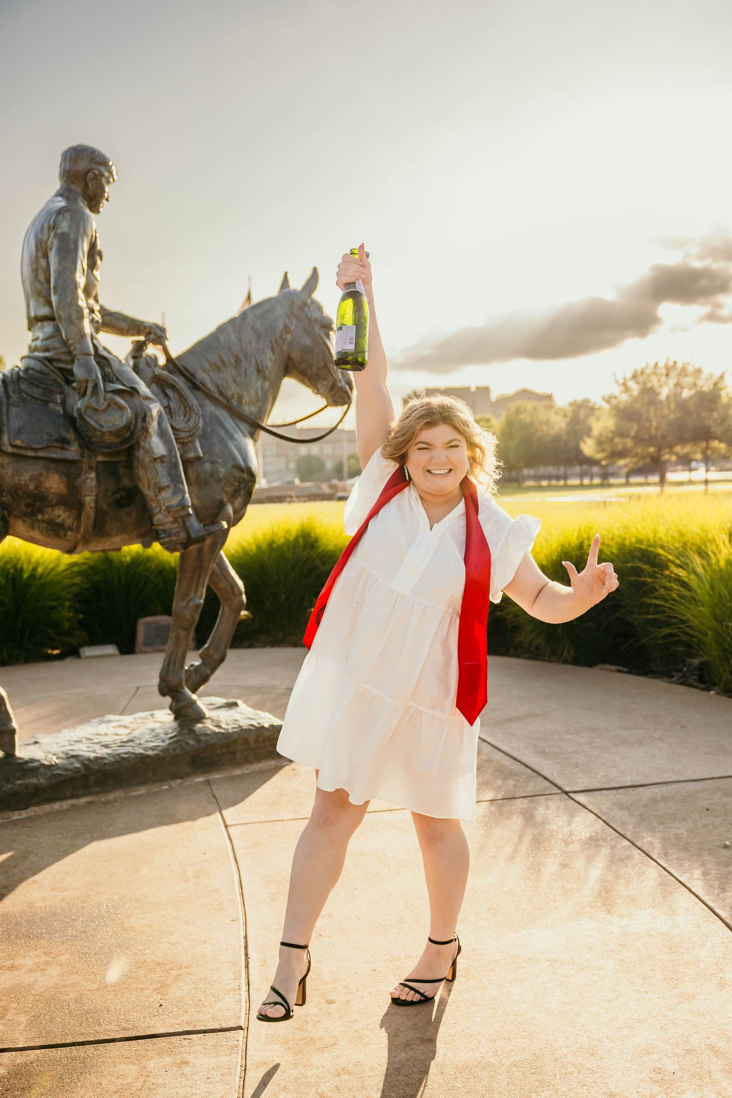 Playful interactions with a bronze statue in a sunlit park during golden hour create whimsical silhouettes against the sky.