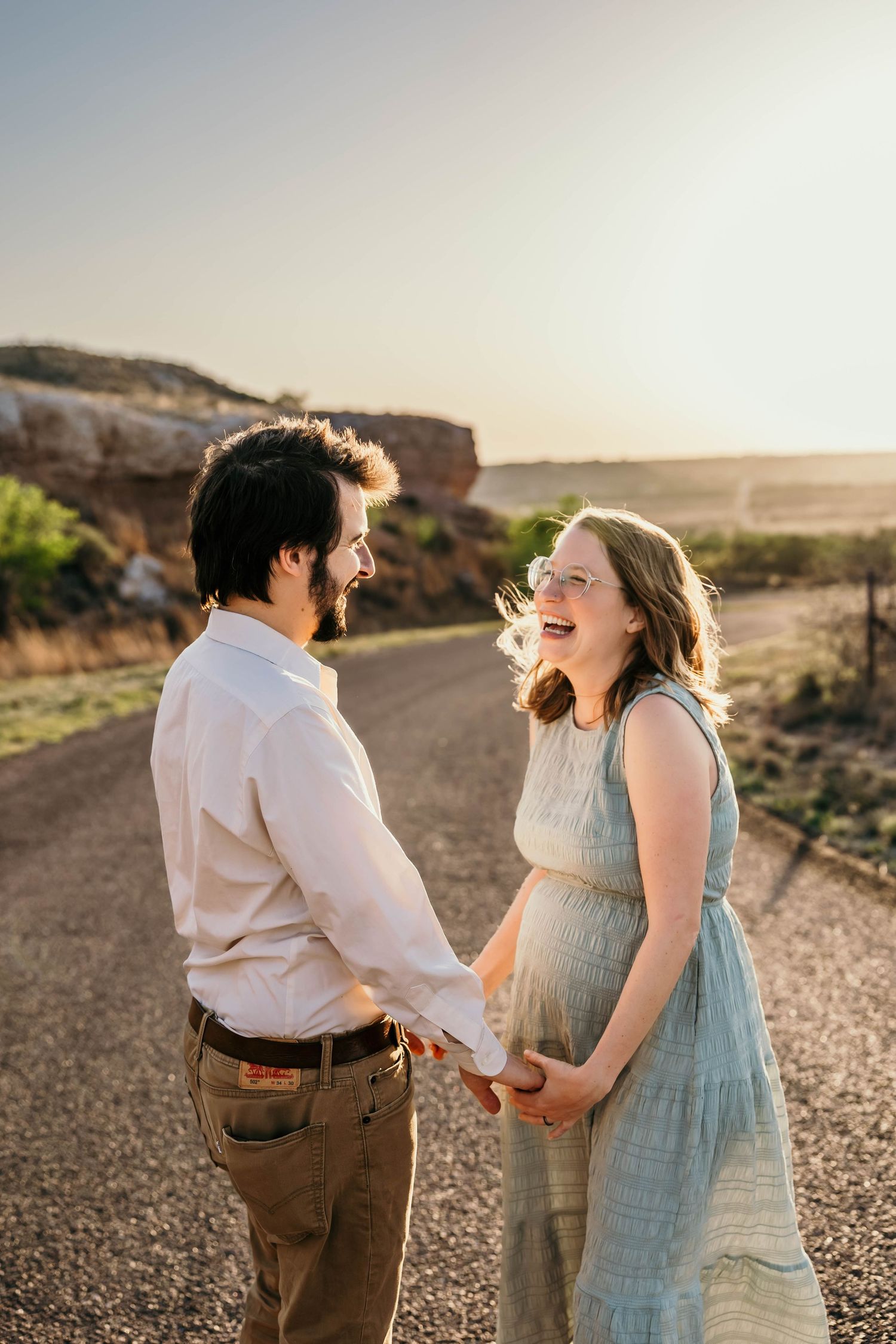Expecting couple shares joyful moment on desert path during sunset photoshoot.