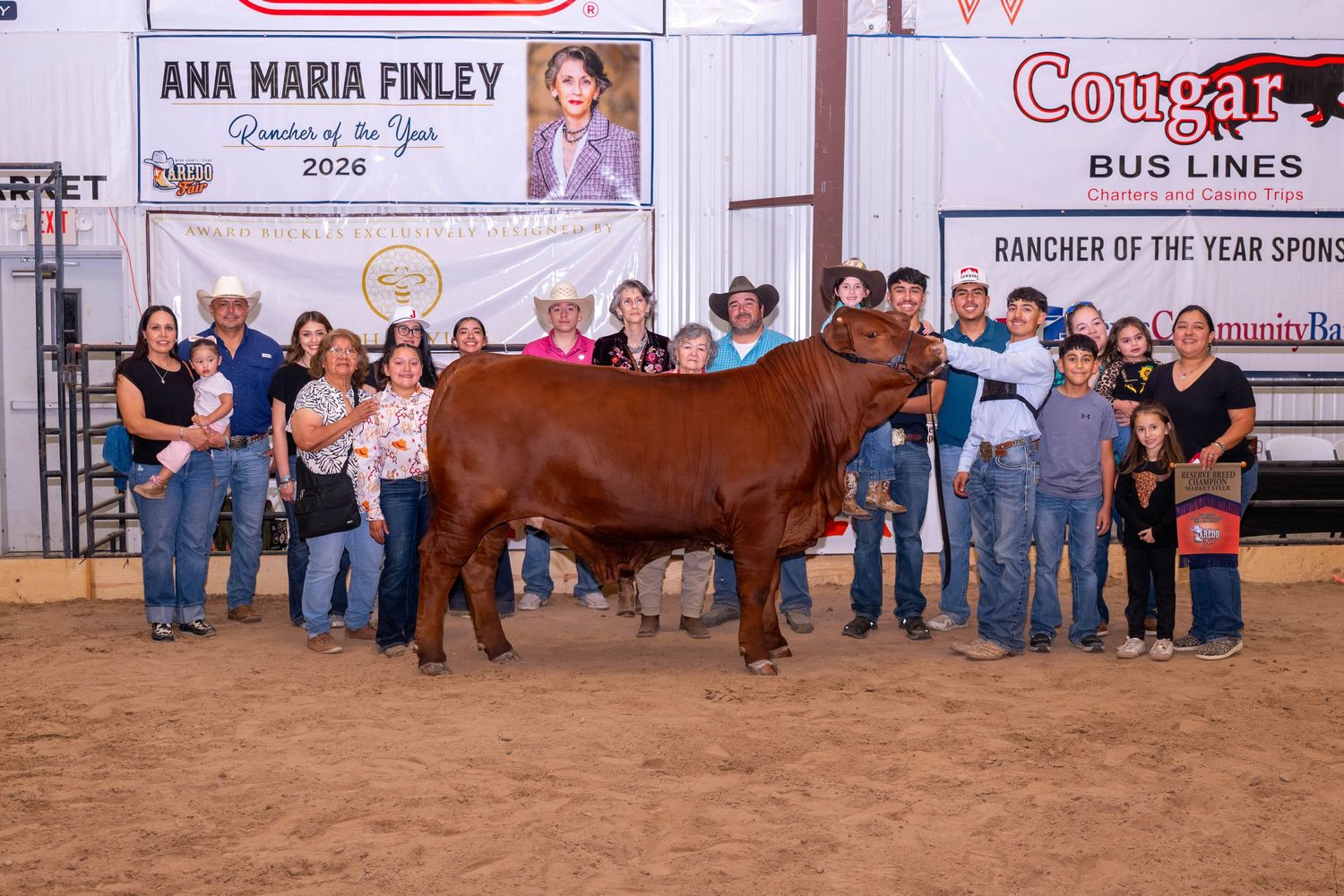Group photo at Ana Maria Finley Rancher of the Year 2026 award ceremony with red bull and Cougar Bus Lines sponsor banner.
