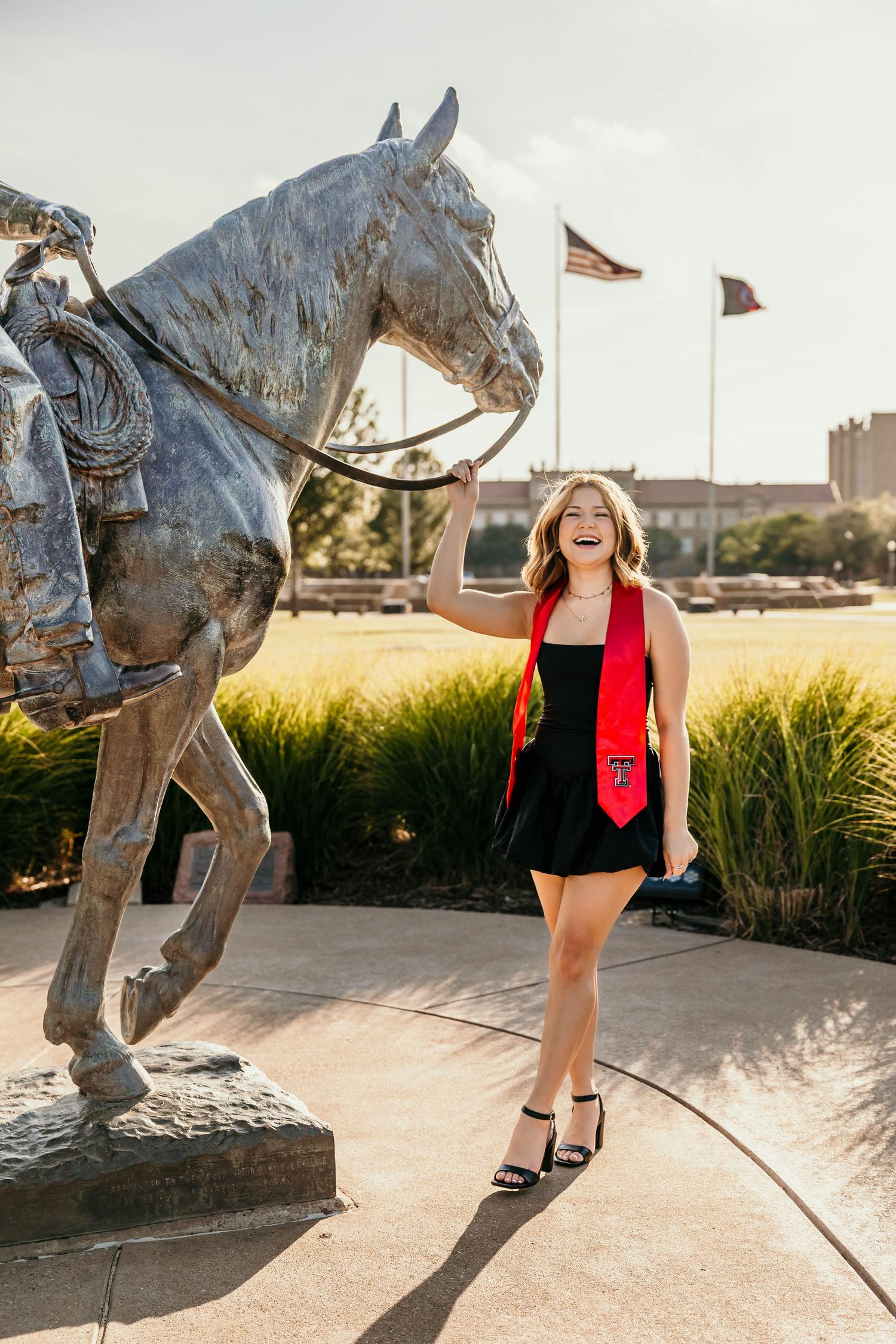 A series of graduation photos next to a metal horse sculpture with brick buildings and flags in the background.
