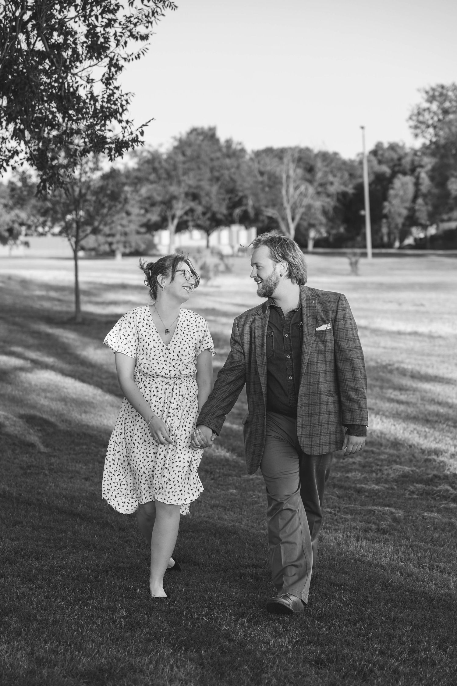A couple in a park walking together, with her in a polka dot dress and him in a plaid blazer in black and white.