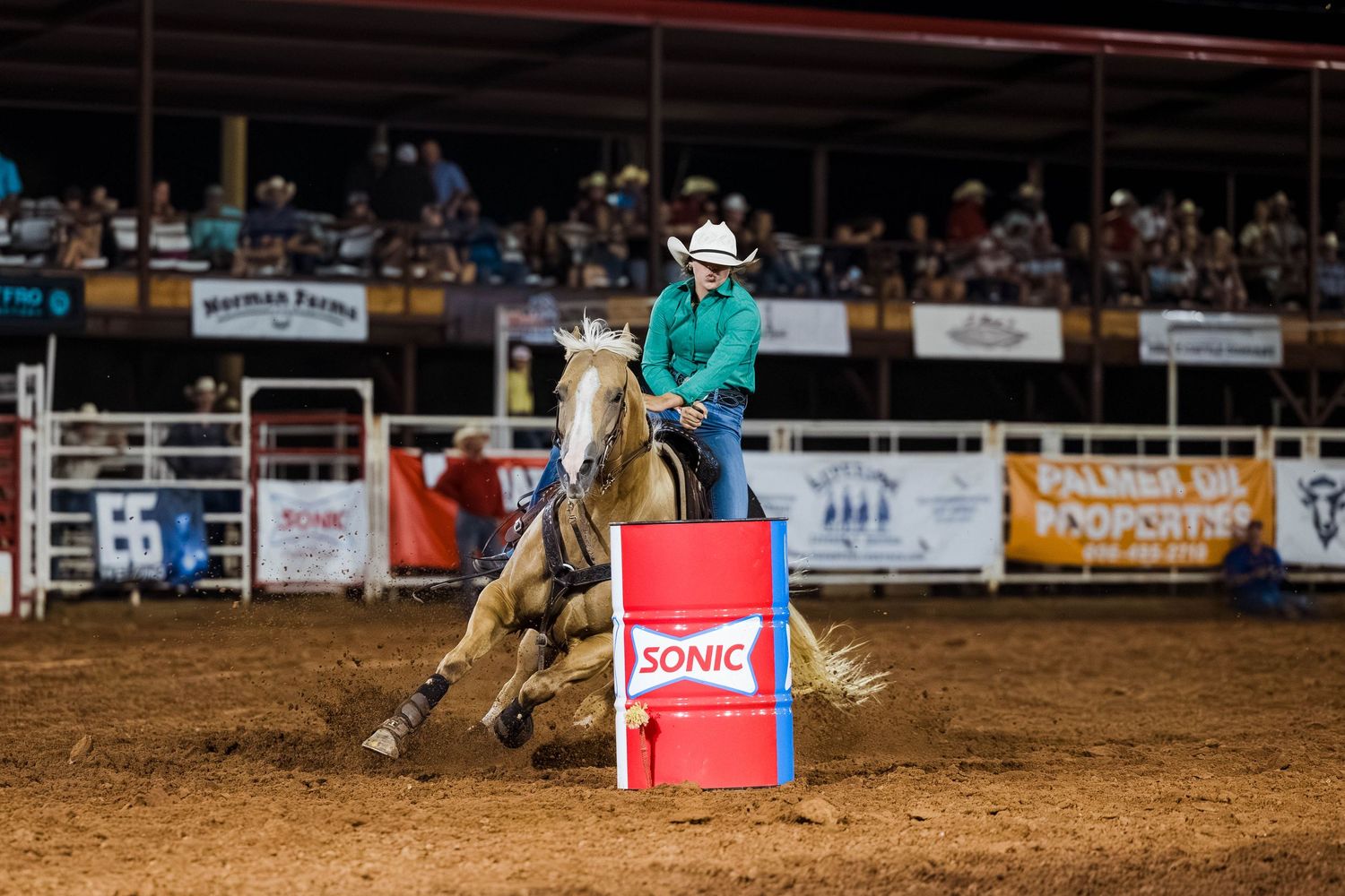 Barrel racing competitor navigating around red barrel in evening rodeo competition.