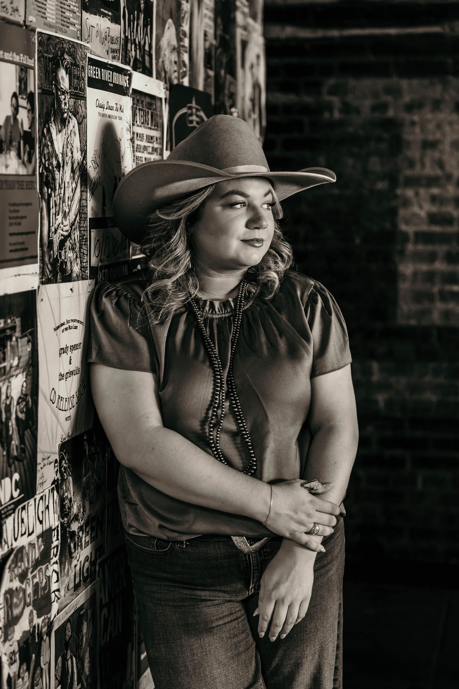 A figure in a stylish hat poses against a black and white backdrop with a moody, vintage aesthetic.
