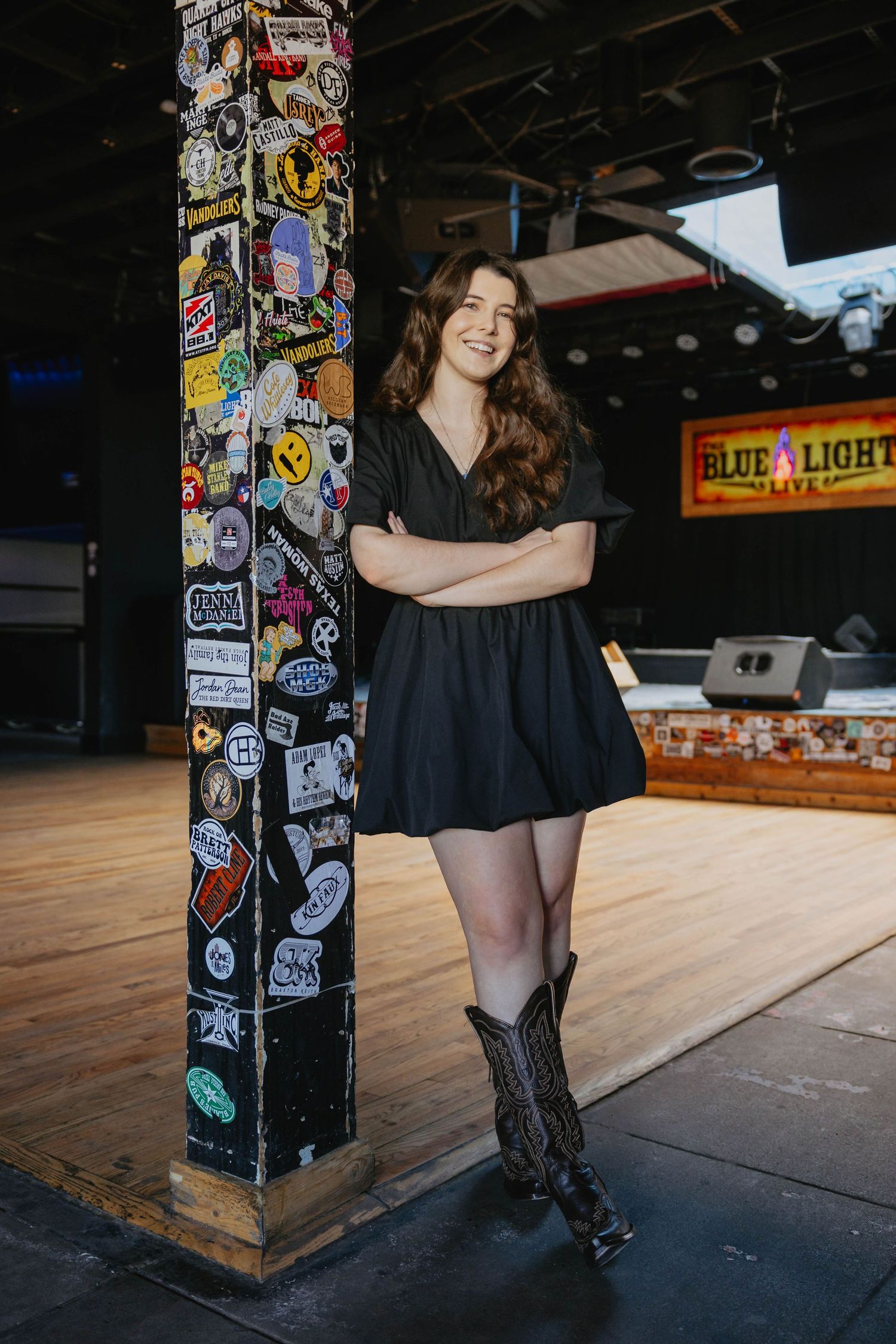 A series of portraits in front of a wooden post covered in stickers at a bar, with black outfit and boots.