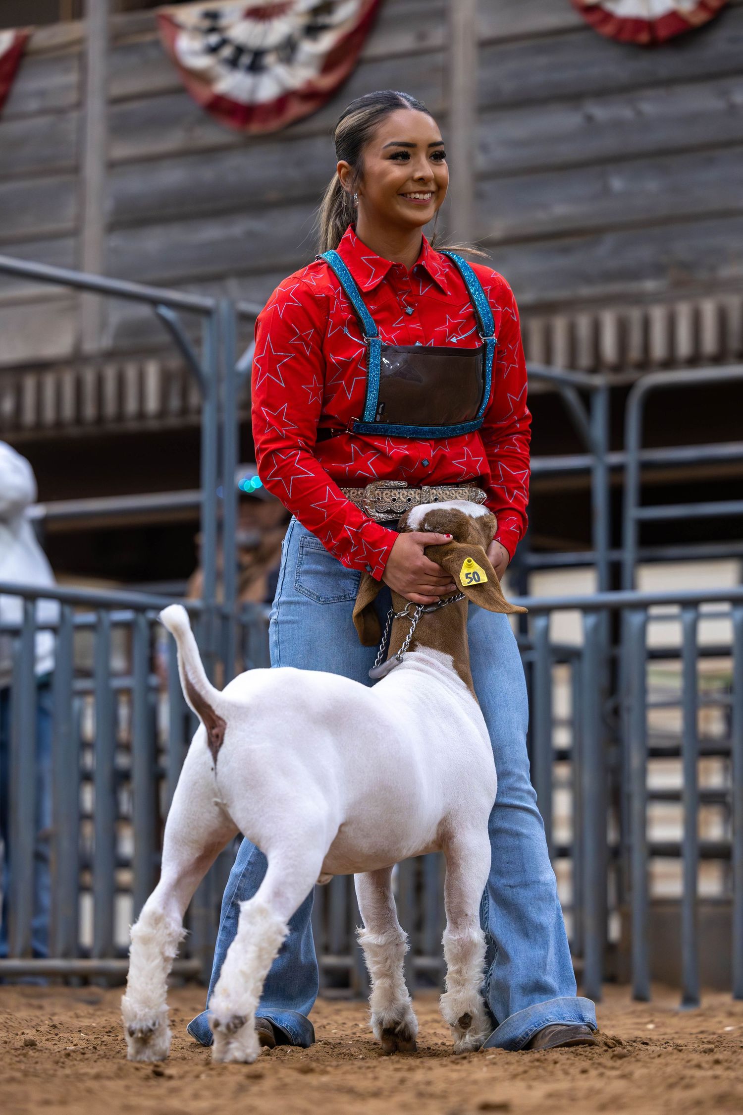 Young exhibitor in red shirt  showing a white goat at a livestock competition.