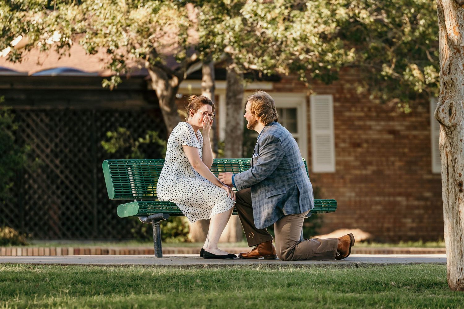 A couple shares a tender moment on a green park bench during a romantic outdoor proposal scene.