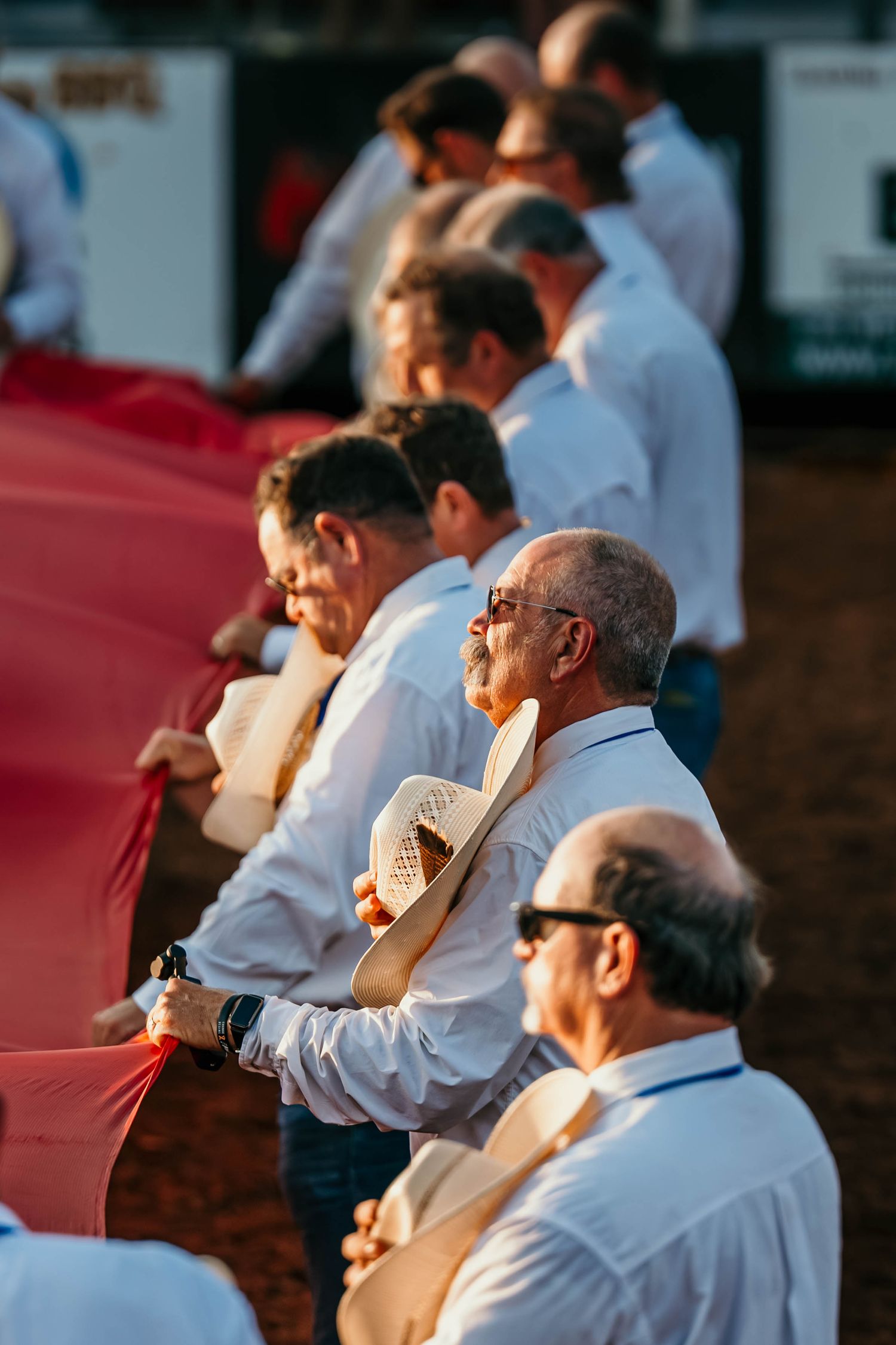 Spectators in white shirts watch intently from the stands during an outdoor sporting event.