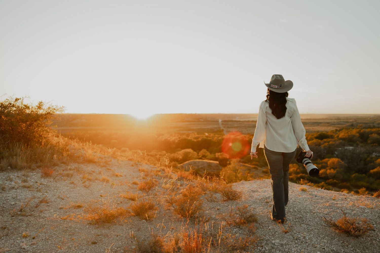 A silhouetted figure walks along a desert trail during sunset.