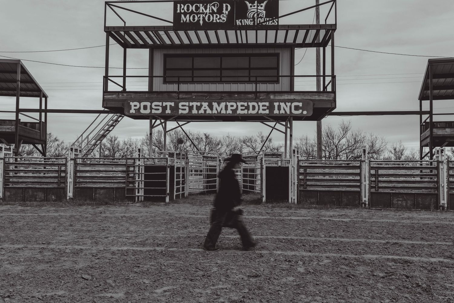 A black and white panoramic photo shows empty rodeo arena gates and fencing at a western event venue.