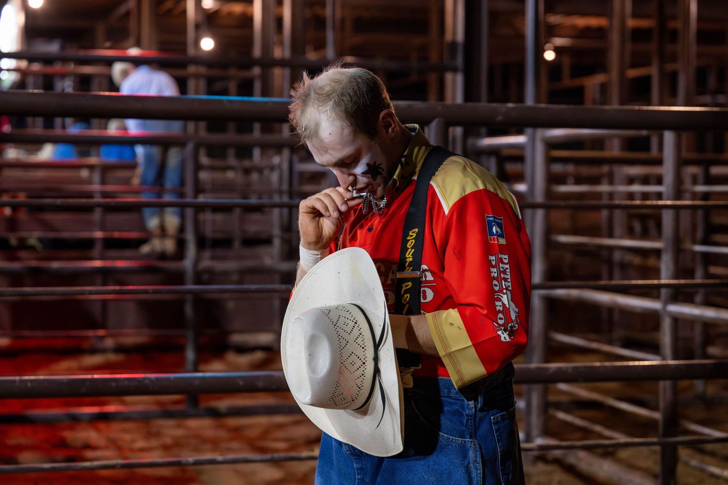 Bullfighter praying and kissing a cross necklace behind the chutes at a rodeo.