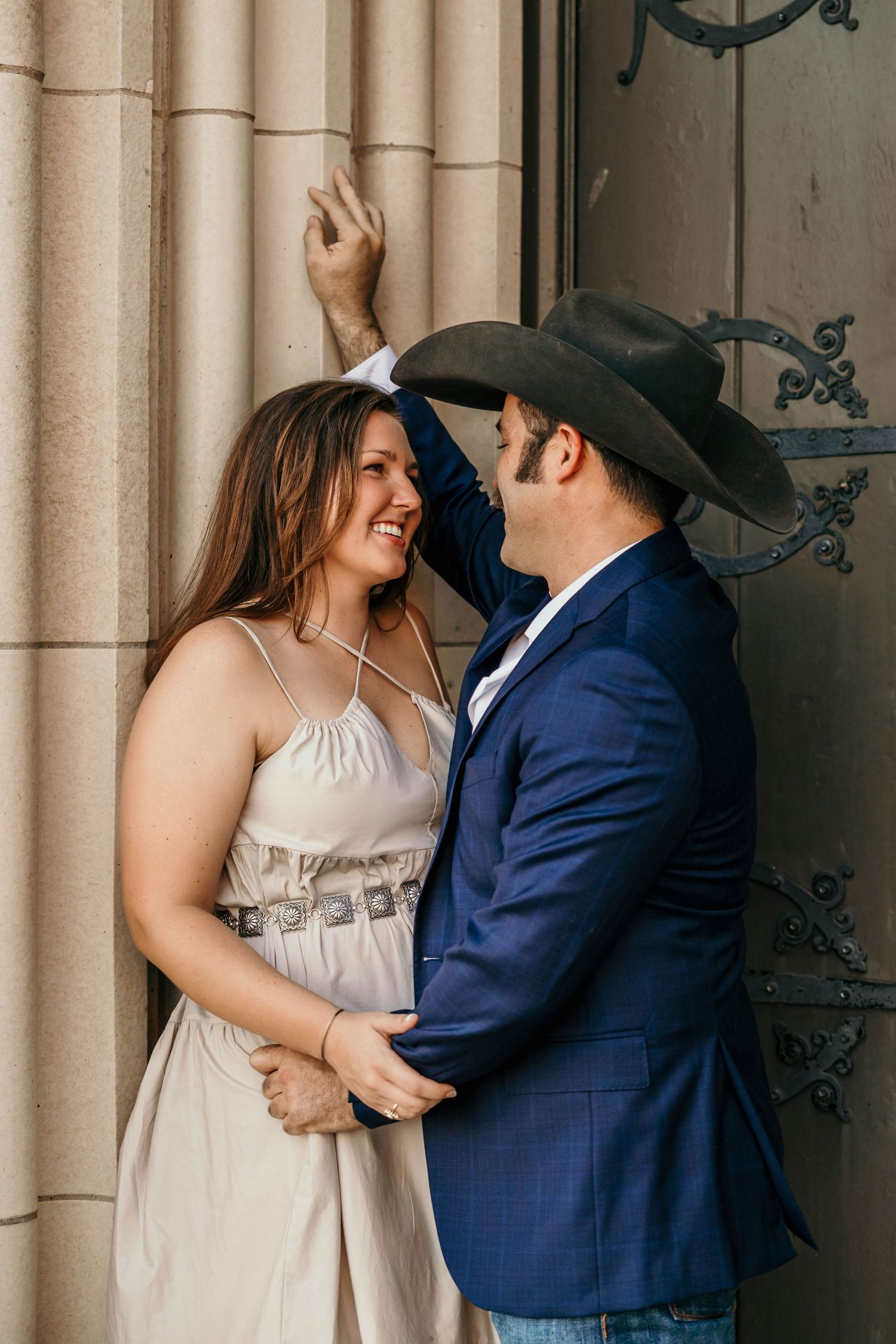 A couple in wedding attire shares a romantic moment against stone columns at their outdoor venue.