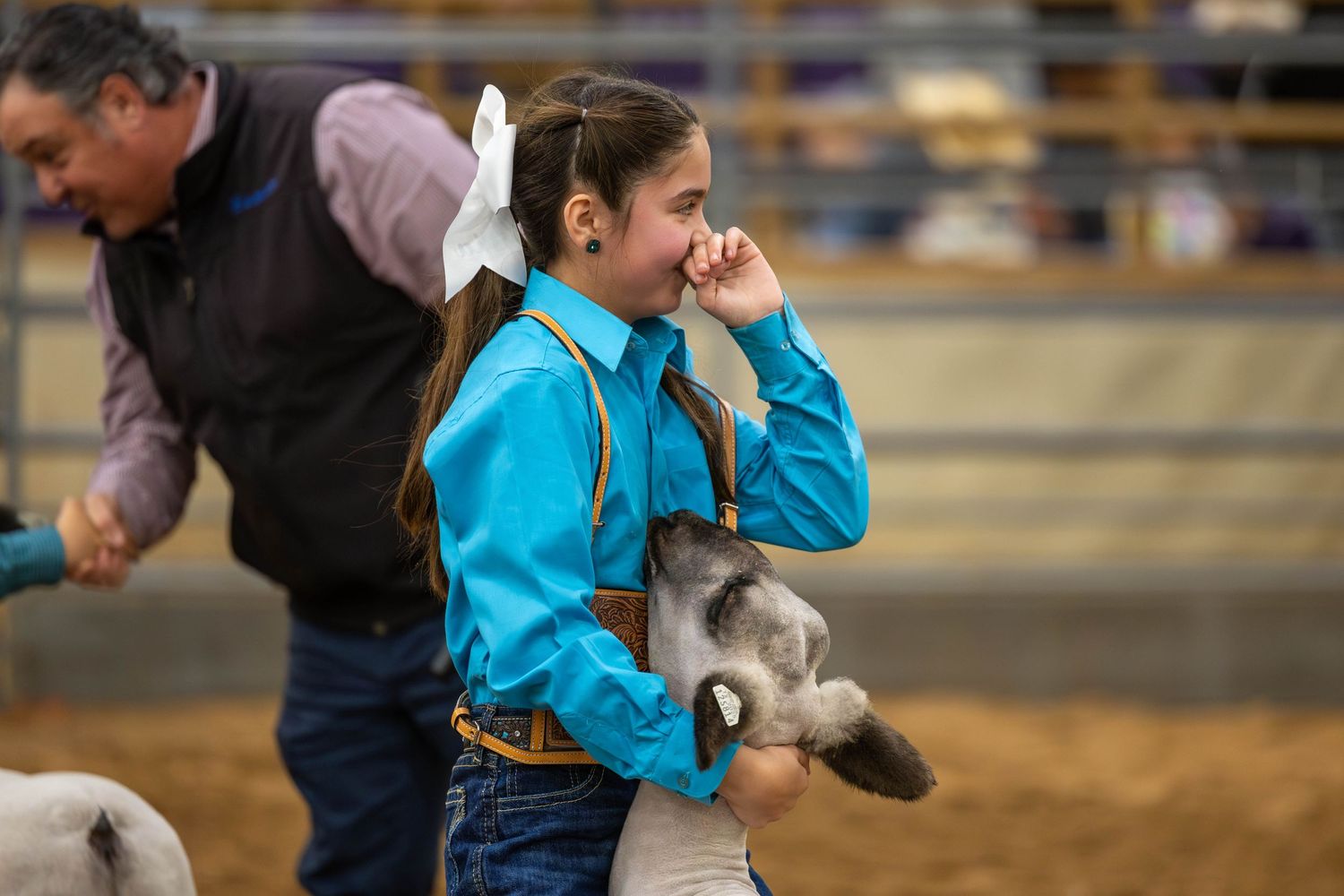 Young competitor in turquoise shirt showing a sheep at an indoor arena event.