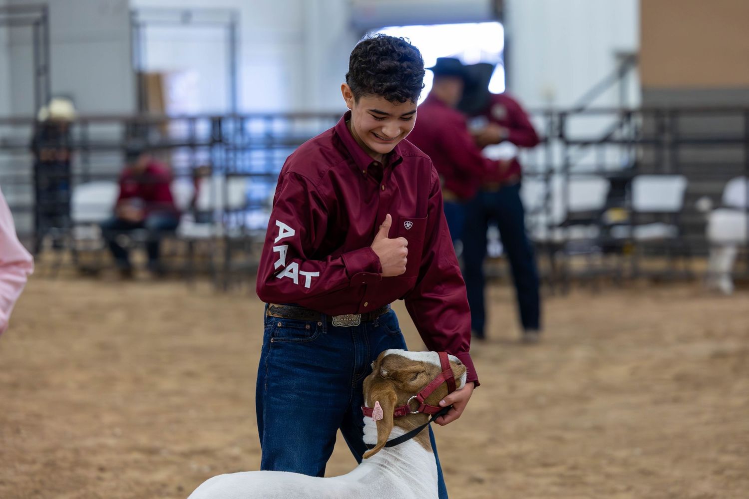 Youth participant in maroon sweater smiles while showing livestock at agricultural competition.