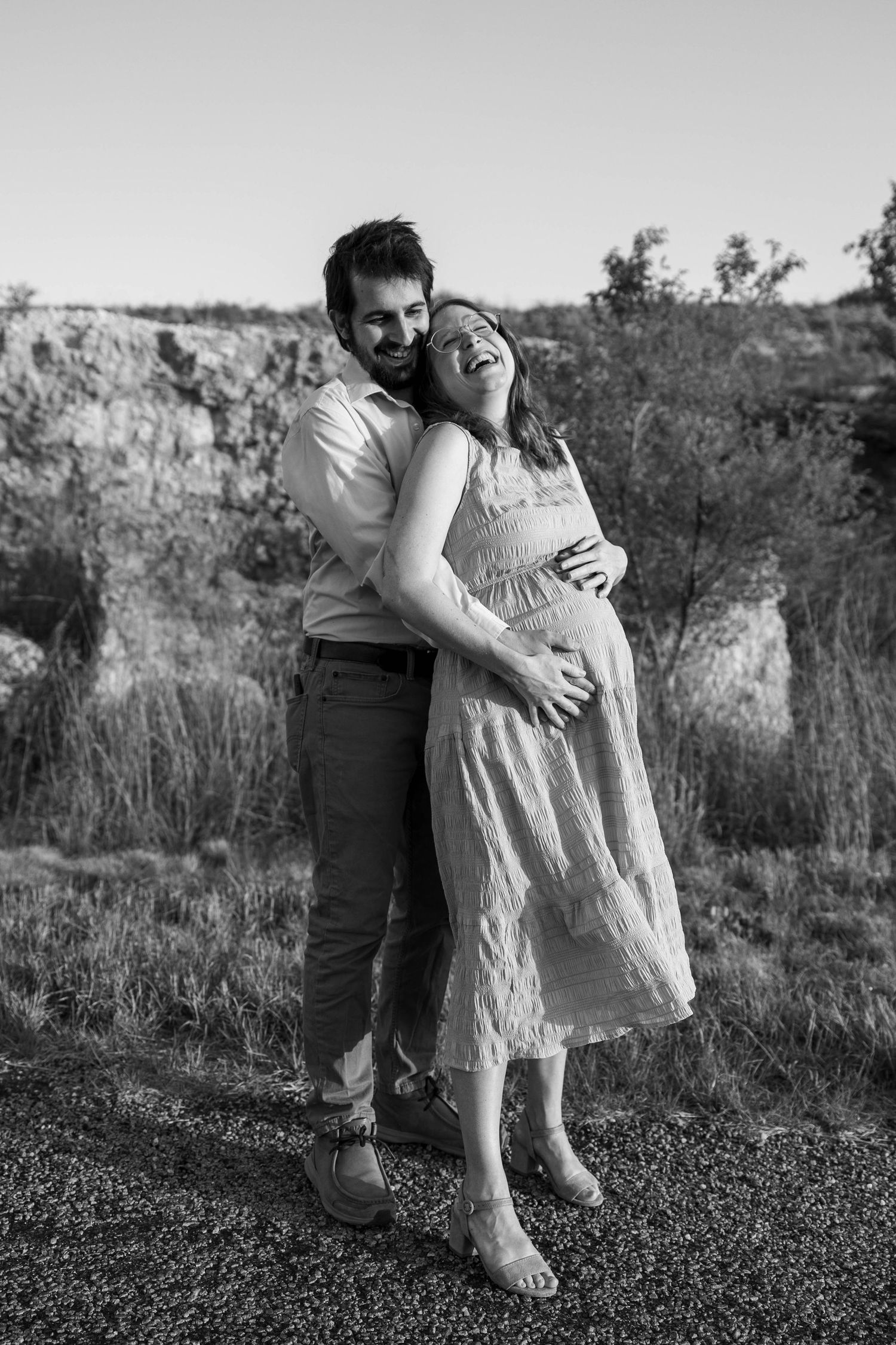 Black and white portrait of expecting couple laughing together outdoors.