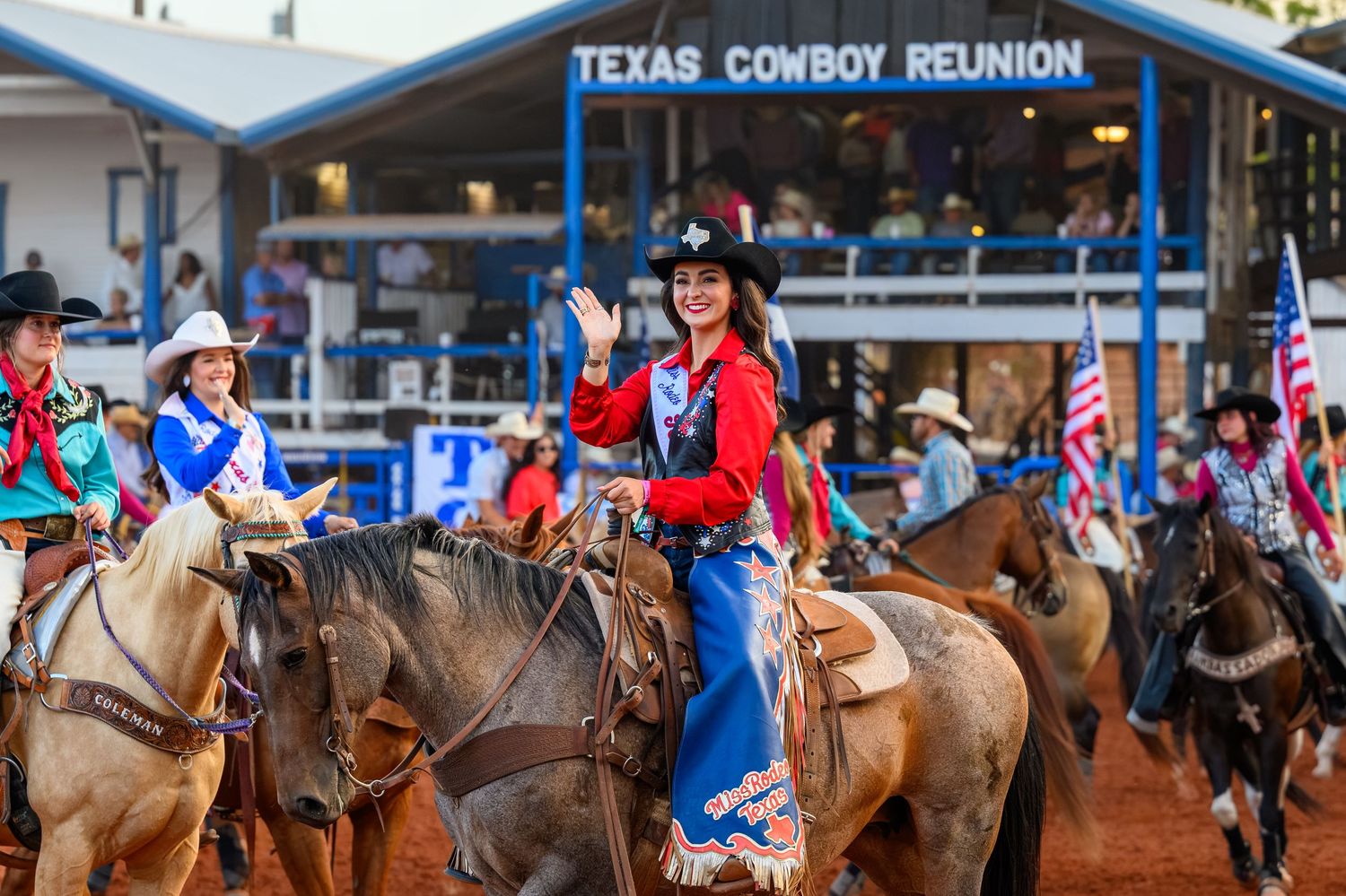 Woman in red shirt waves on horseback at Texas Cowboy Reunion rodeo parade with riders and American flags.