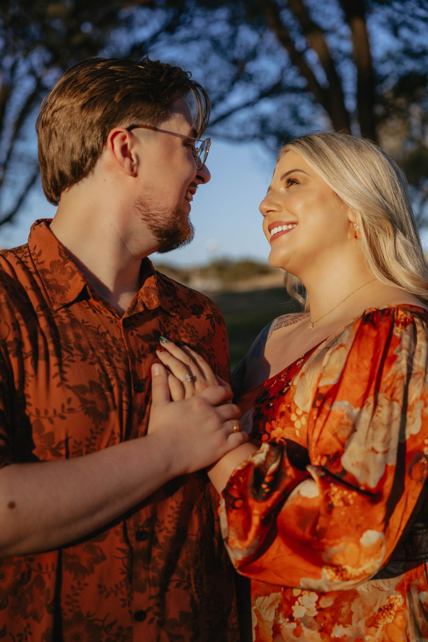 A couple wearing matching orange and red patterned outfits share an intimate moment at sunset.
