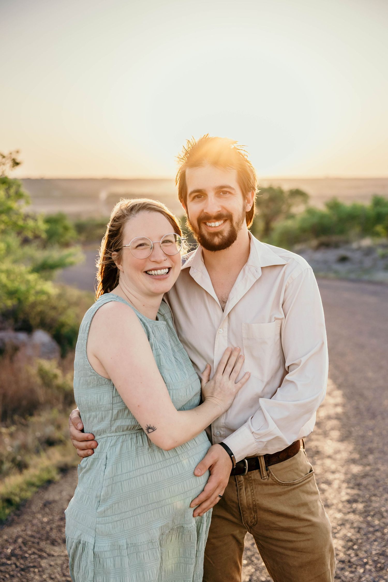 Candid sunset portrait of expecting couple smiling on desert trail.