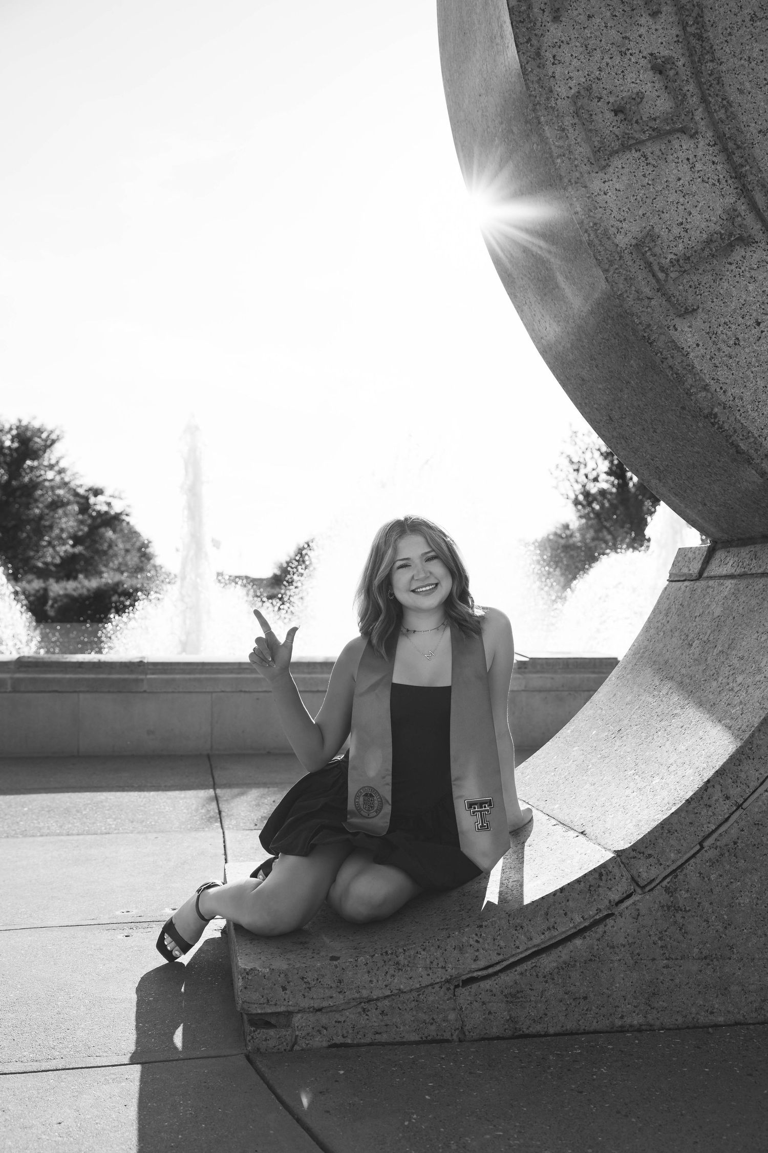 A black and white photo of someone sitting on a curved stone structure with the Washington Monument visible in background.