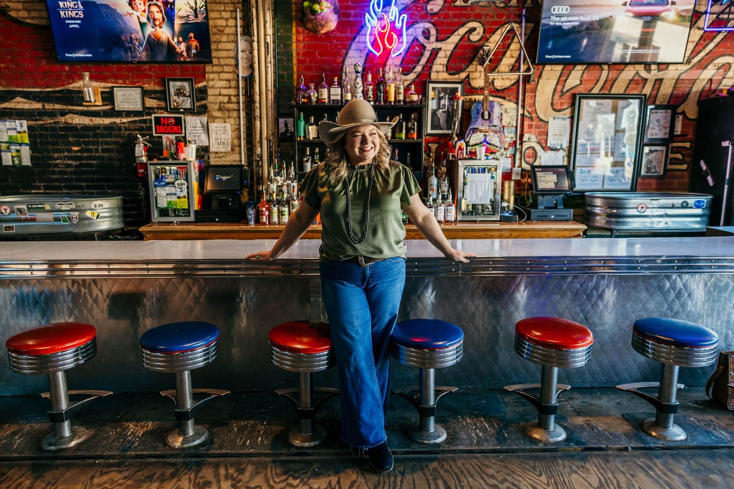 Panoramic view of red bar stools along a dimly lit bar counter with neon lights in the background.