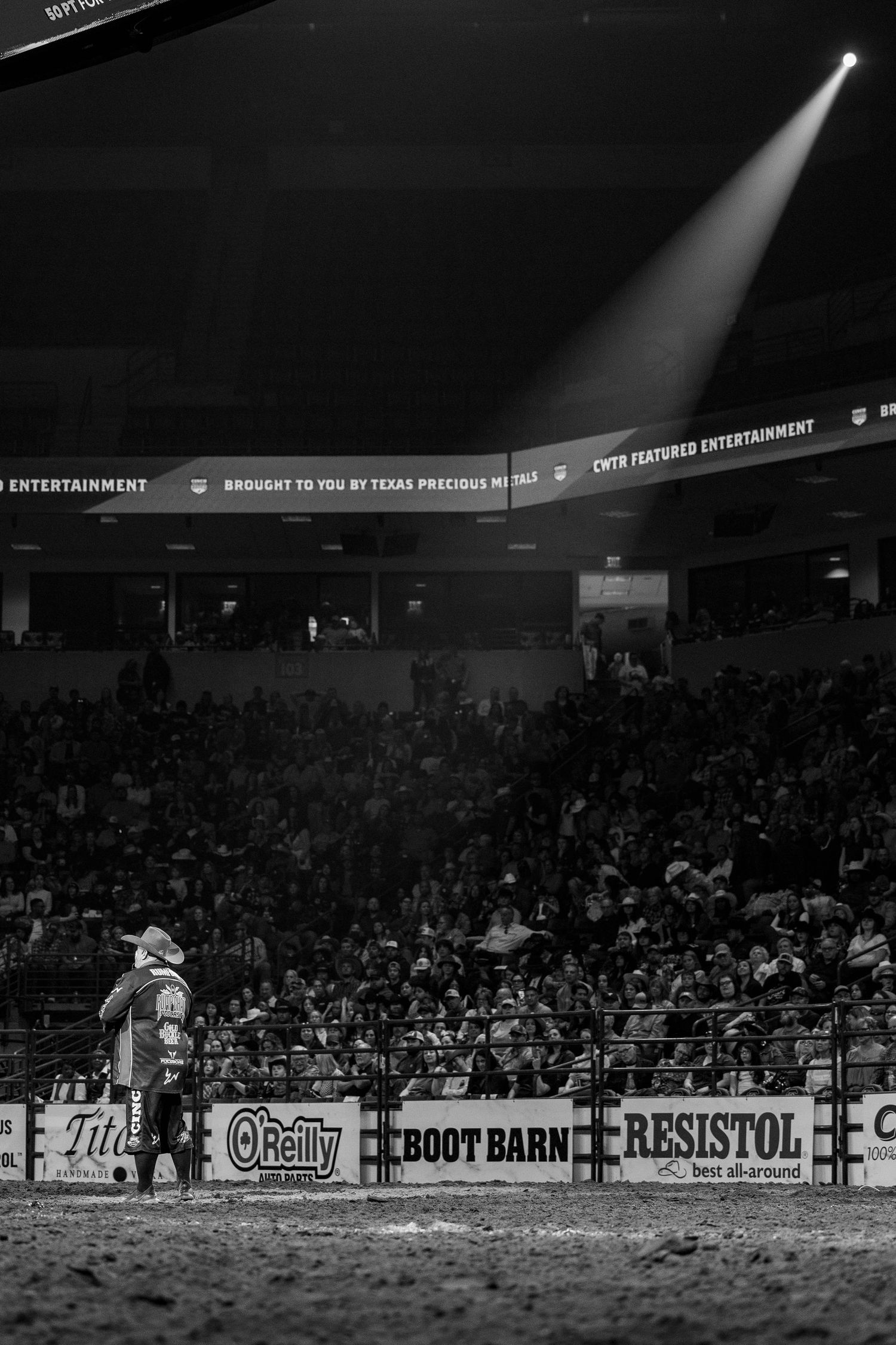 A spotlight illuminates Justin Rumford standing in a darkened rodeo arena.