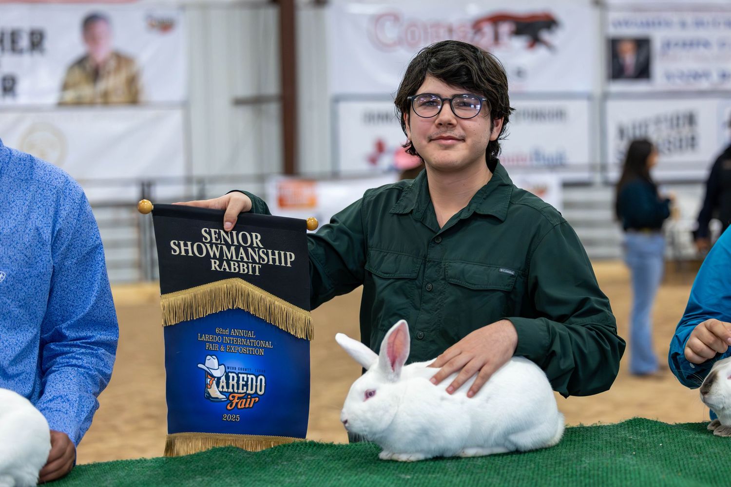 Youth participant with award banner displaying white rabbit at livestock competition.