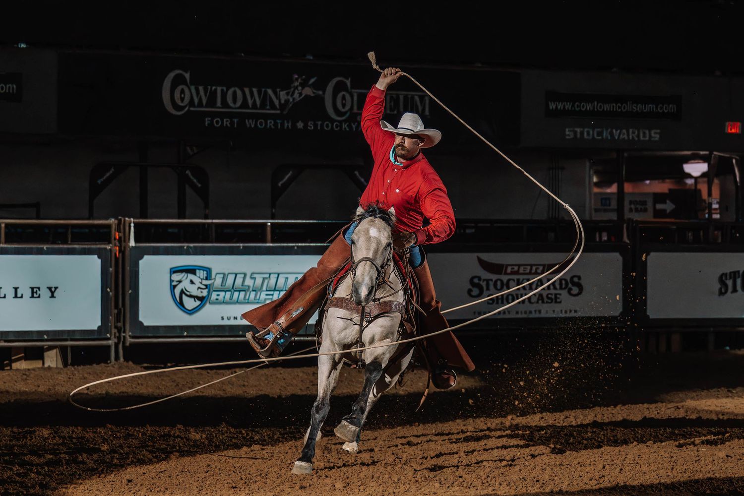 Cowboy demonstrating roping skills on horseback during nighttime rodeo performance.