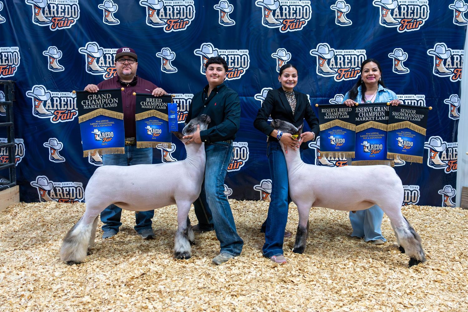 Exhibitors displaying prize-winning lambs at livestock show with sponsor backdrop.