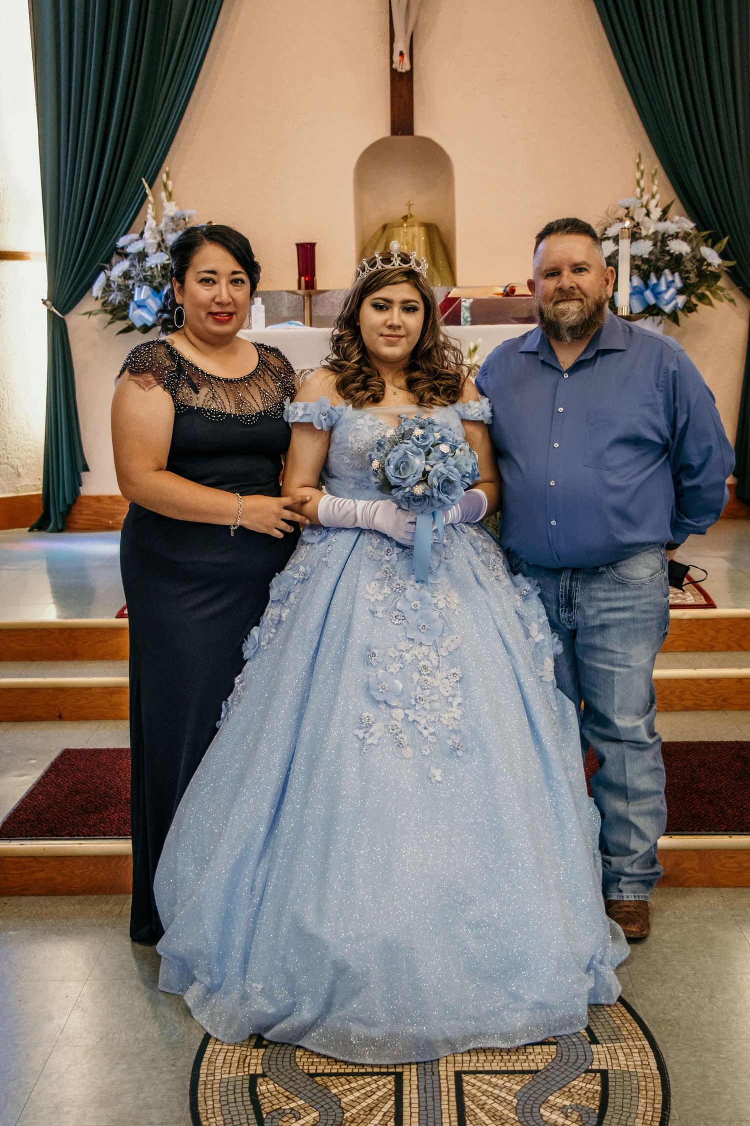 A quinceañera celebration in a church featuring a light blue ball gown with lace details and blue floral decorations.