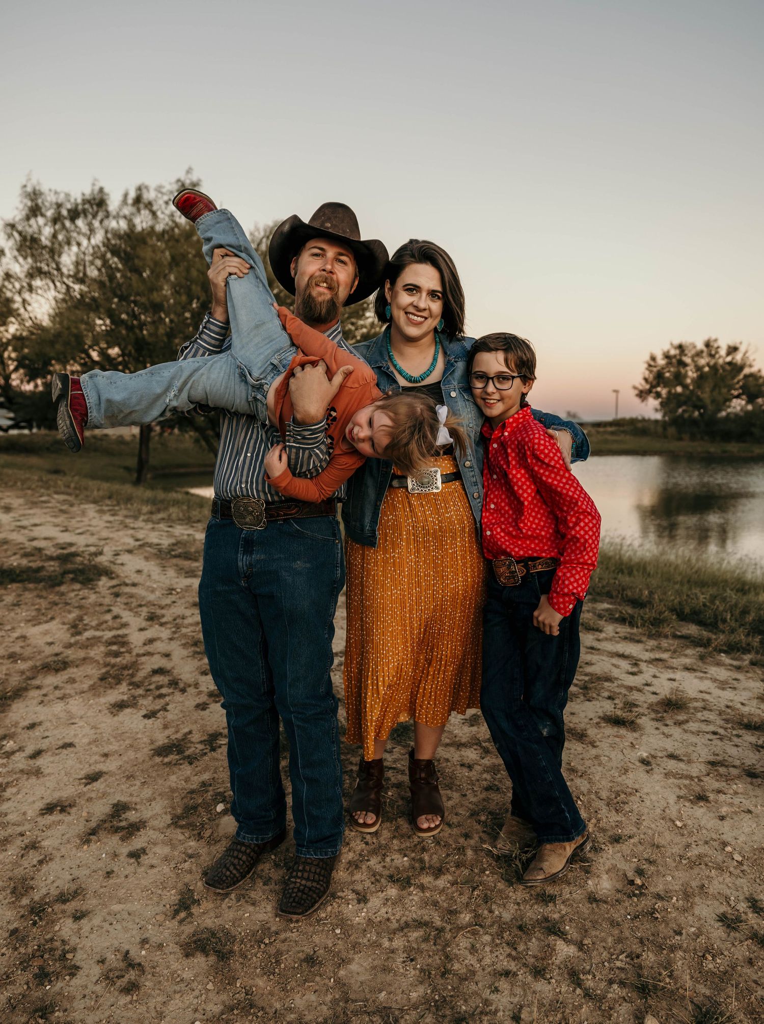 A western-themed family photo shoot outdoors at sunset with cowboy attire and playful poses.