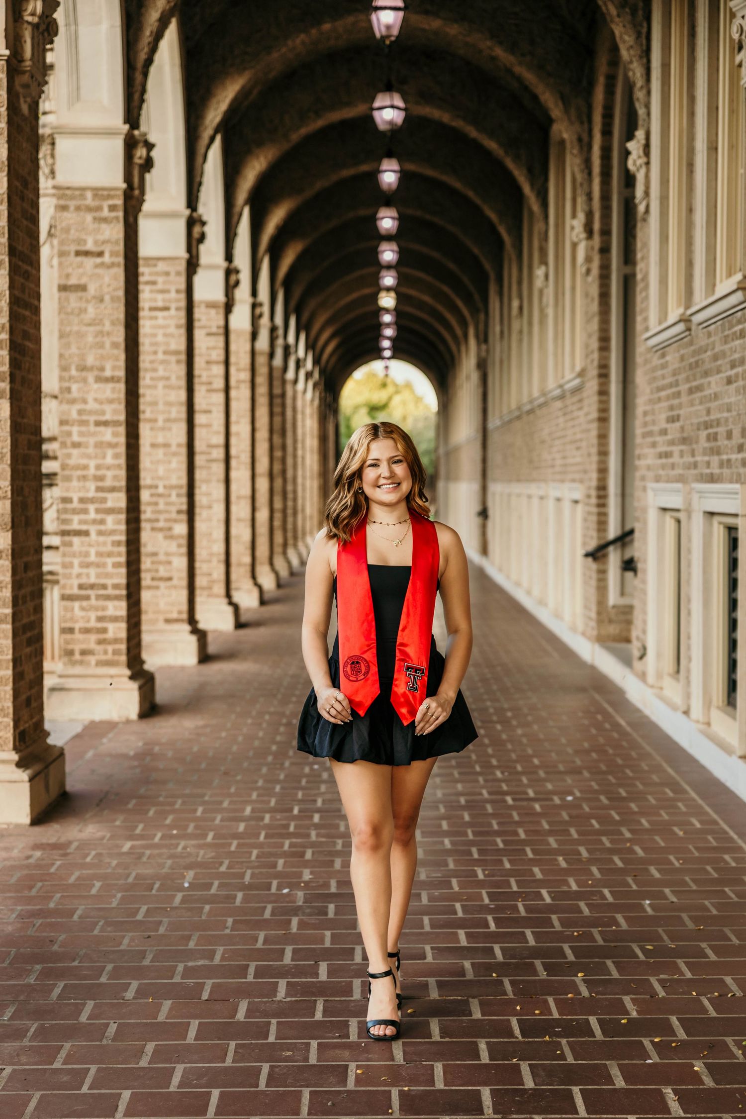 Graduation photos taken in an arched brick colonnade with decorative lighting and architectural details.