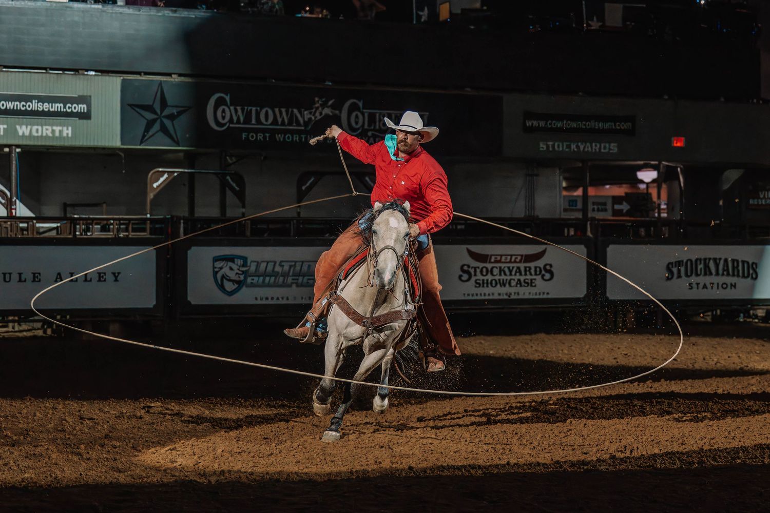 Cowboy on white horse swinging lasso at Cowtown Stockyards rodeo in Fort Worth, Texas.