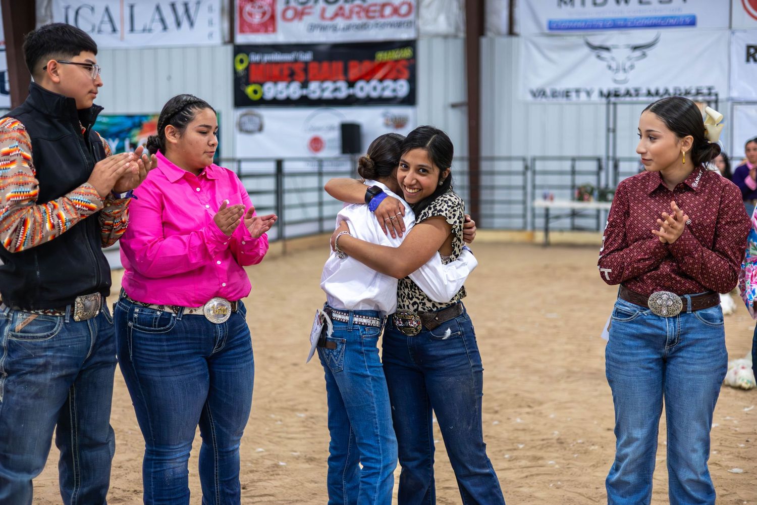 Group of people in western wear gathering and chatting in a livestock arena.