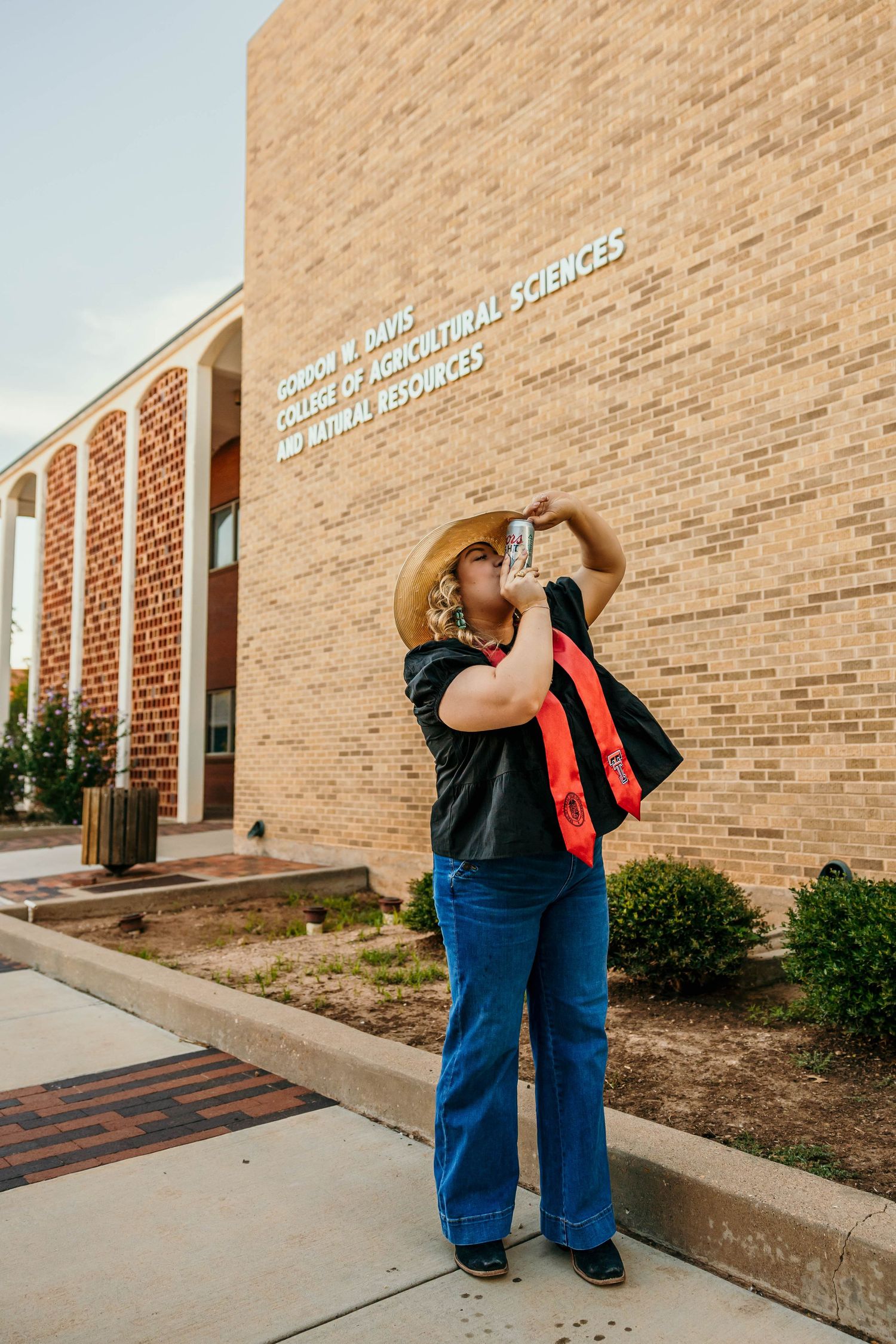 Someone in jeans and a dark shirt takes a photo outside a brick academic building for agricultural sciences.