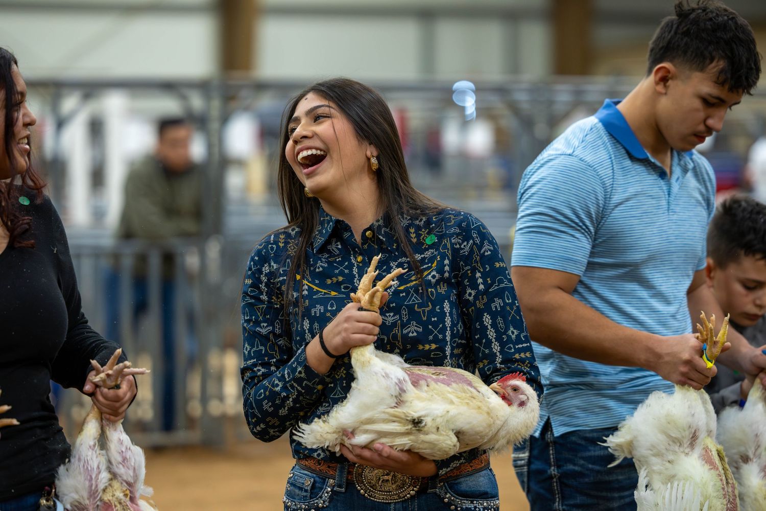 Participants sharing laughs while holding chickens at an indoor livestock show