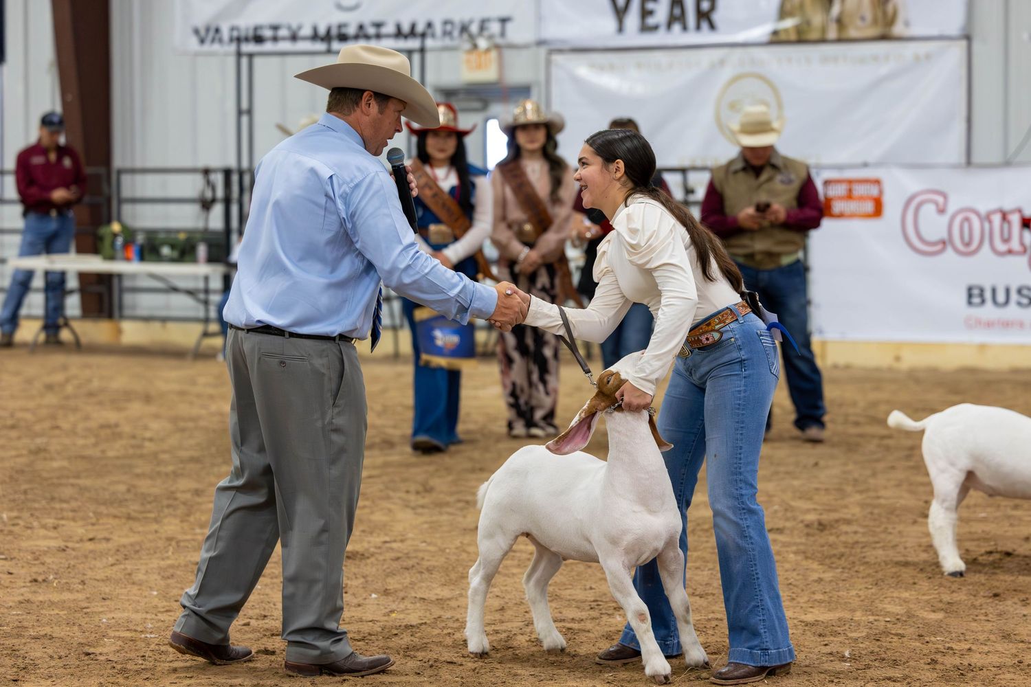 Participants present their goats for judging at a livestock show competition in a dusty arena.