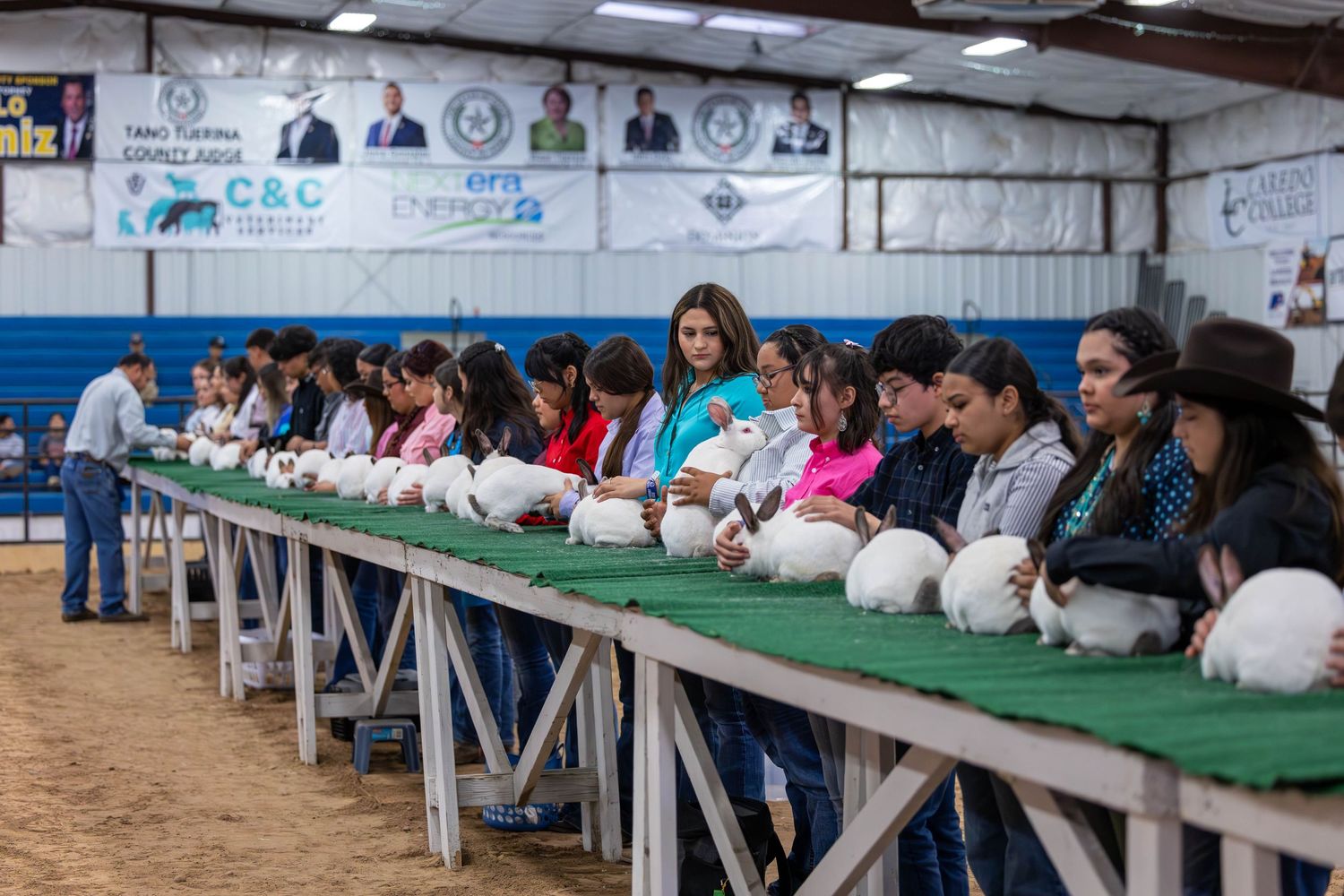 Students sit at a long table with white helmets lined up at a livestock show or agricultural education event.