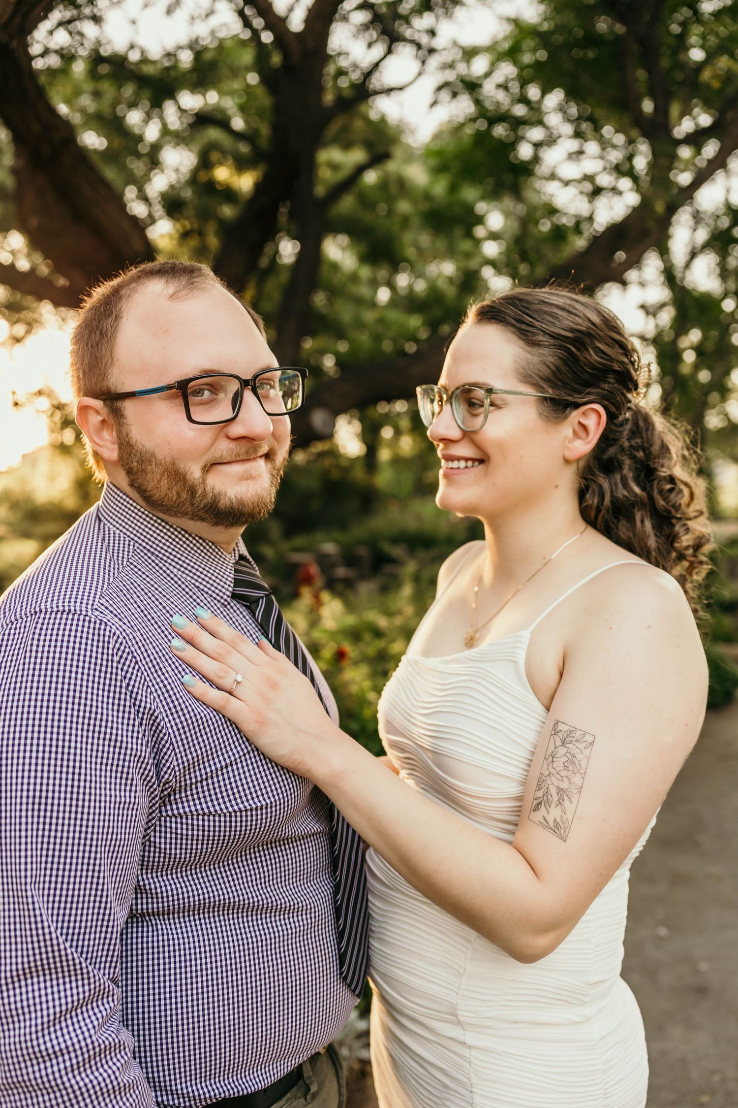 A couple in wedding attire share a tender moment at sunset, with trees creating a natural backdrop.